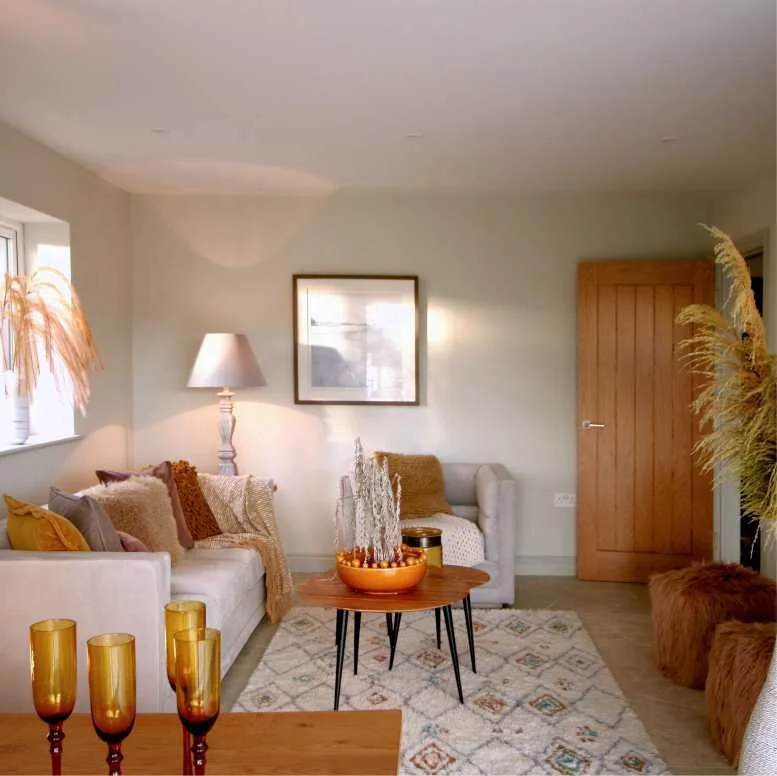 A neutral and beige lounge with lots of textured accessories in brown, ochre and yellow.  Real grasses, patterned rug and lots of cushions in wool, faux fur, velvet and cotton are on the three seater sofa and a chair.  Two poufs complete the scene
