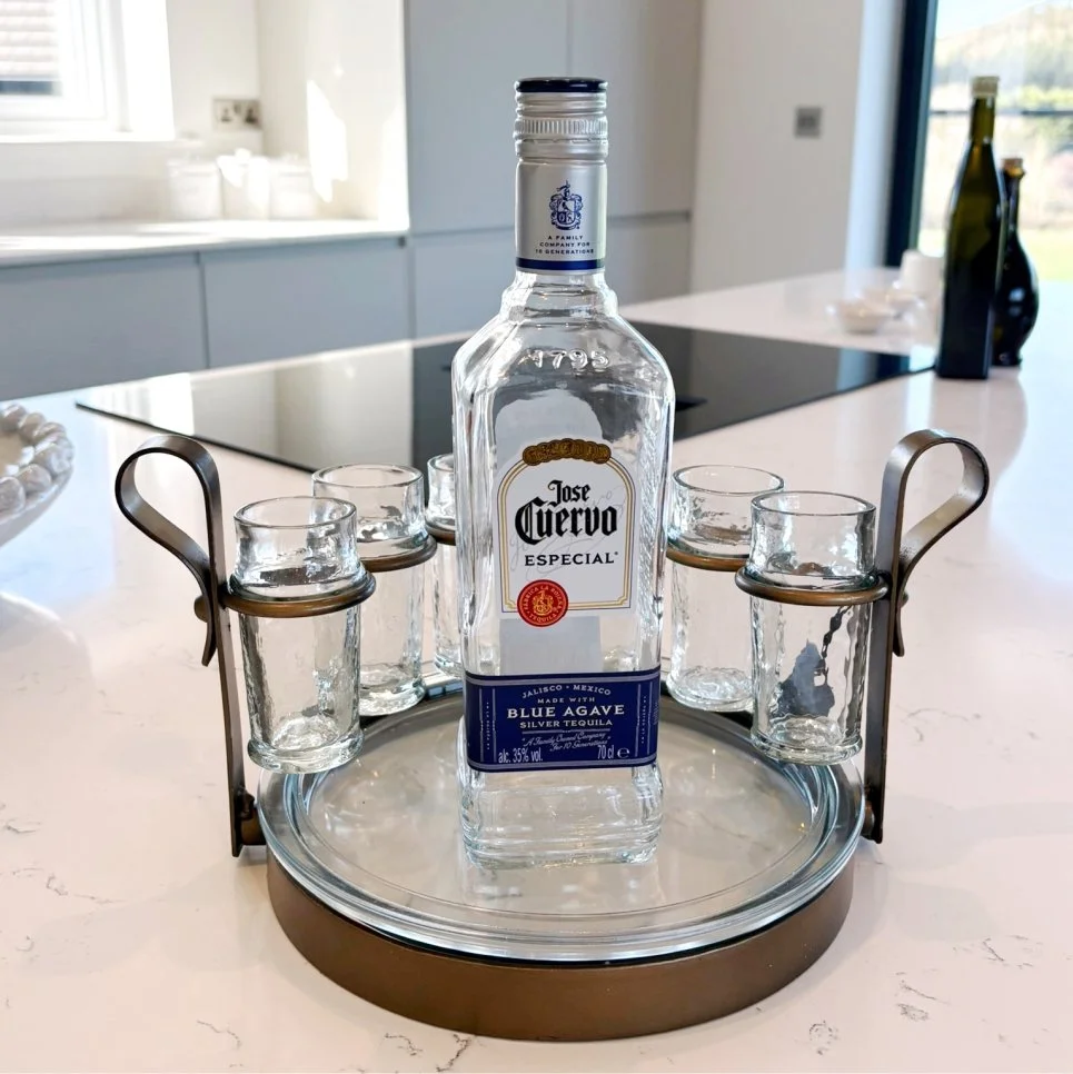 6 shot glasses are suspended on a metal frame.  On a tray sits a tequila bottle