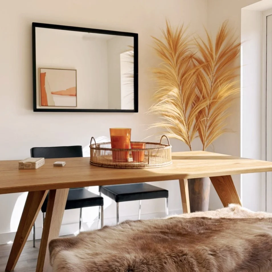 a modern oak dining table with a casual fur bench and orange candles and picture.  There is a tall grass decoration