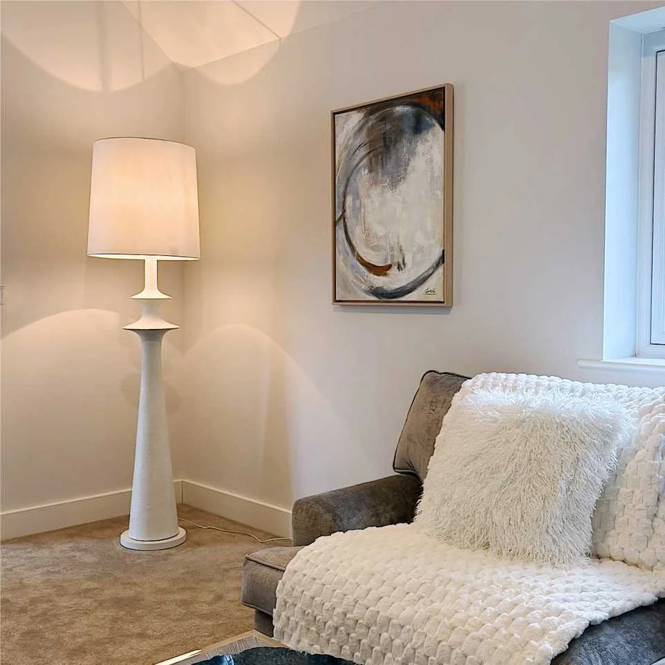 contemporary lounge with large white floor lamp, abstract wall art and grey velvet sofa with white throw and faux fur cushion