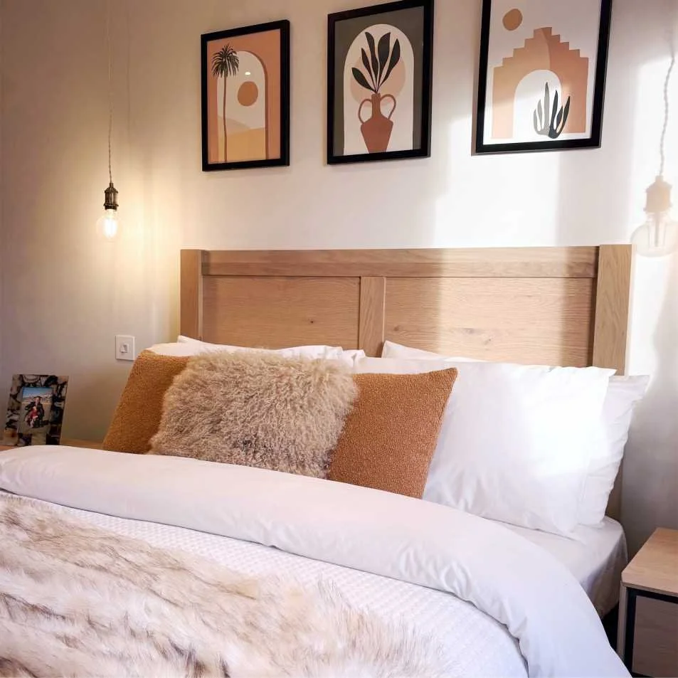 Bedroom with wood panel headboard and bed dressed with luxury fur throw and fluffy cushions.  The neutral scheme is reflected in the pale brown and light orange graphic prints which have a moroccan quality