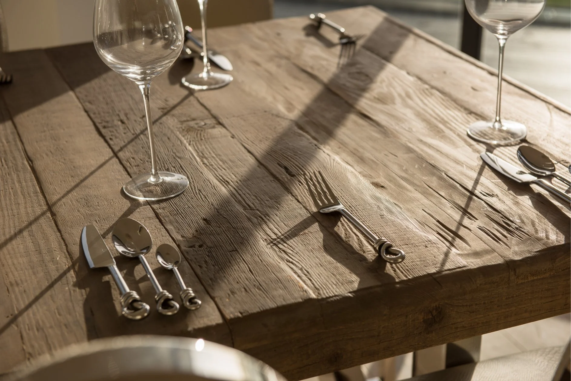 a highly textured wood table features knot cutlery and large wine glassese