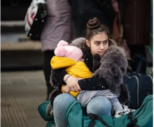 Young mother holding child on lap sitting in crowded area with suitcases