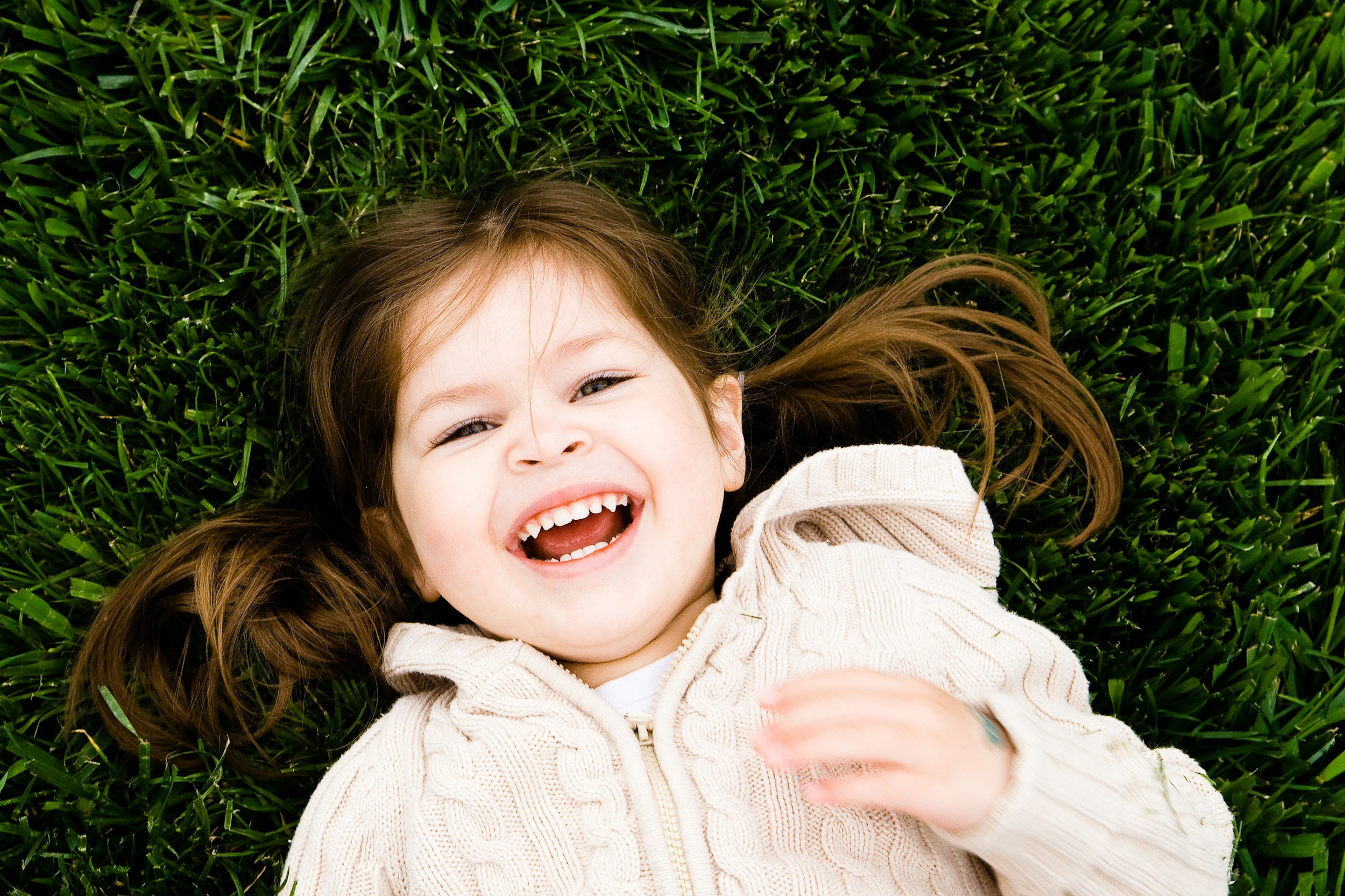 young girl with brown hair laying on the grass smiling