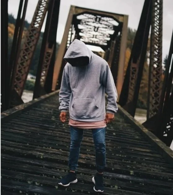 Teen boy with grey hoodie standing on railroad tracks staring down
