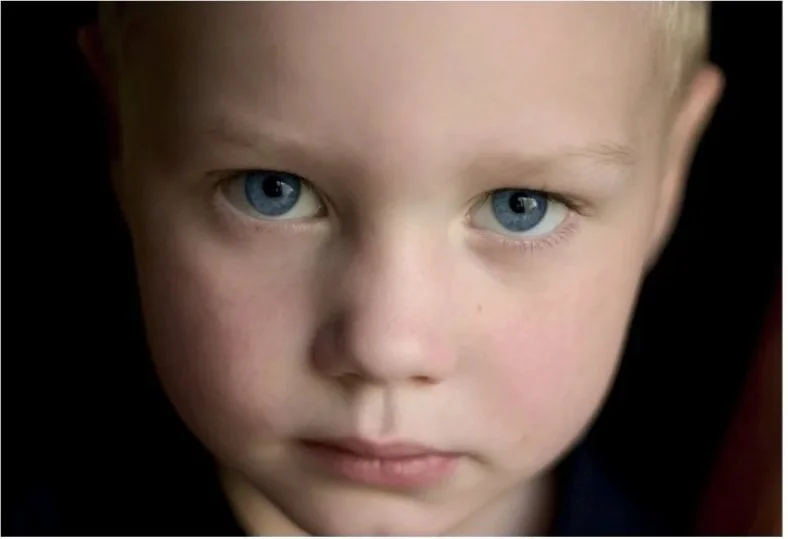 Blond haired young boy with blue eyes staring at camera