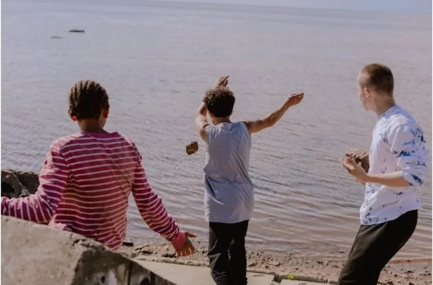 Three teen boys throwing rocks into a lake