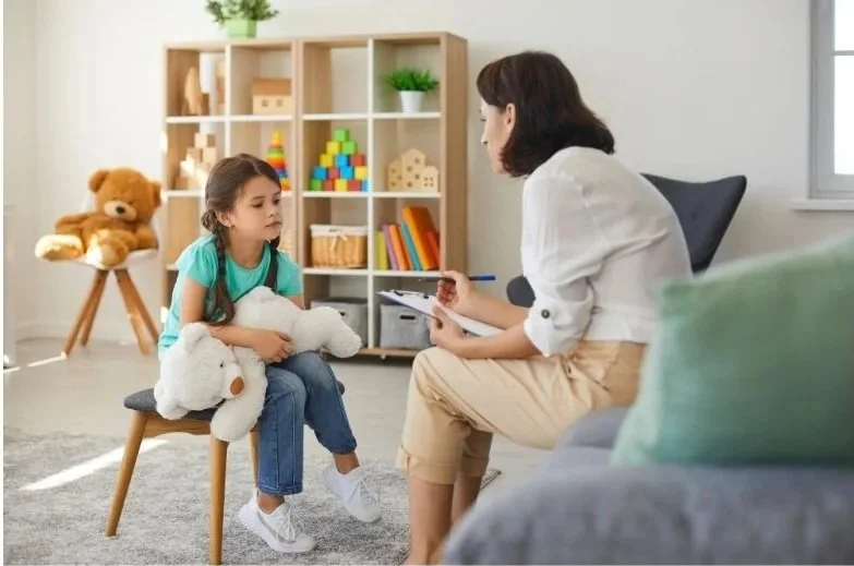 Adult woman interviewing a young girl holding a white teddy bear in a