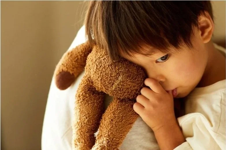 Young asian boy with teddy bear sucking thumb