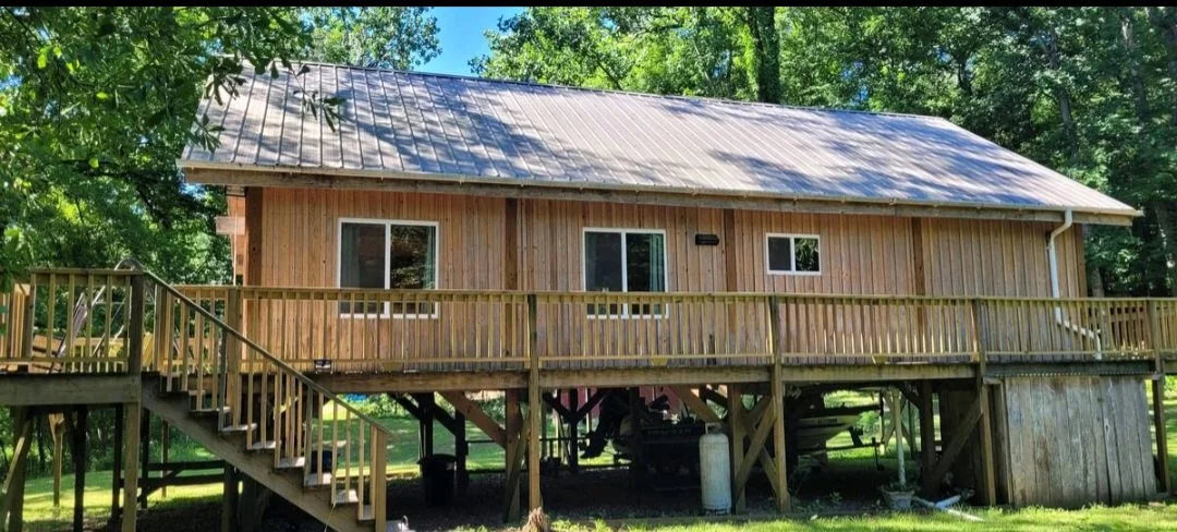 A wooden house with a metal roof raised on stilts surrounded by green trees.
