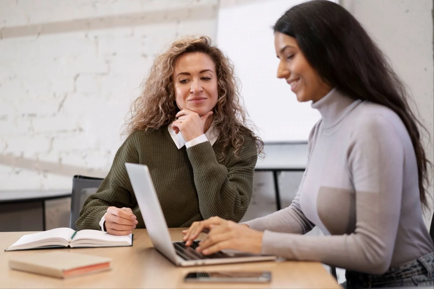 Two women working together at a desk looking at a laptop