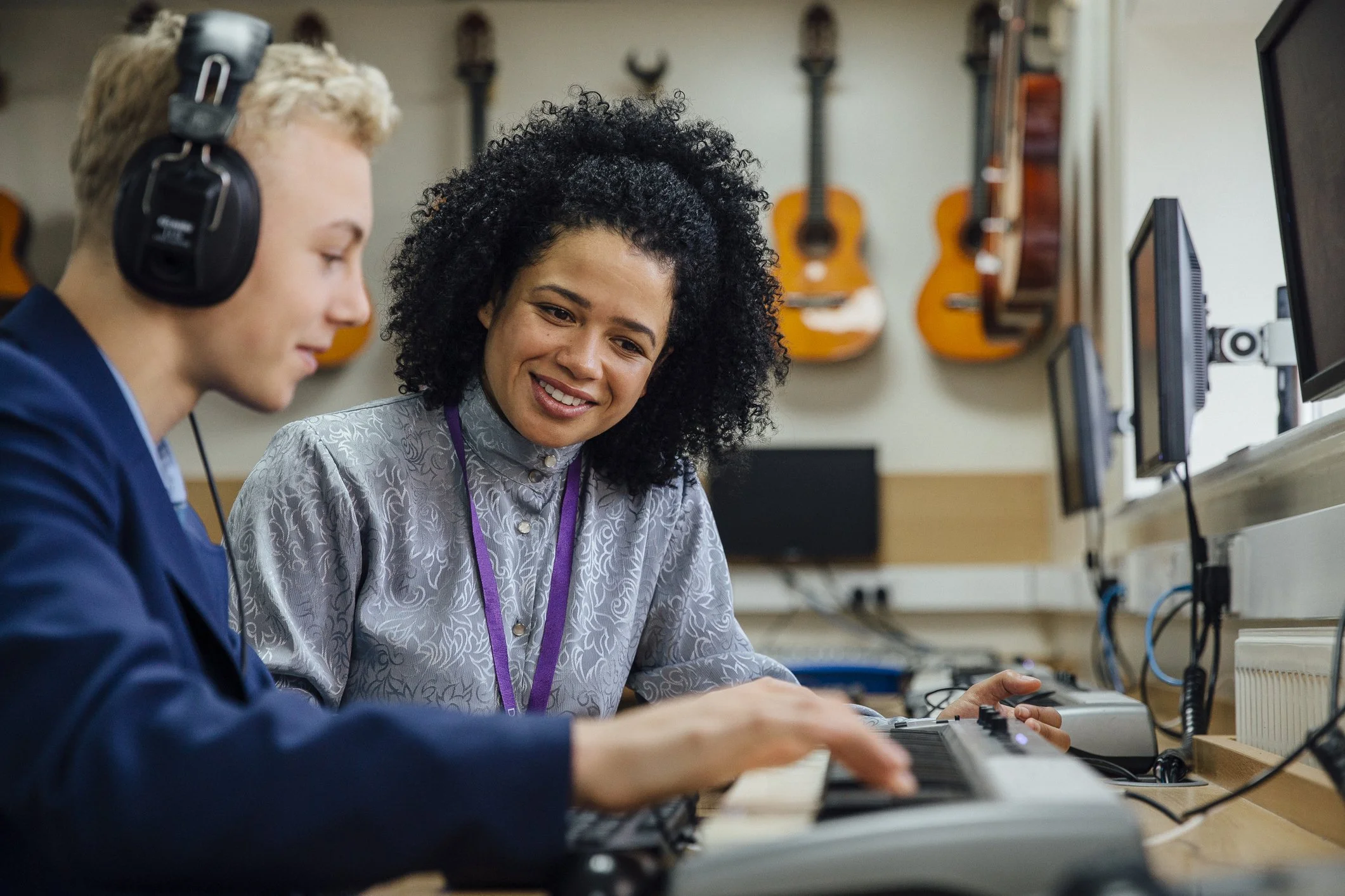 Two people operating audio equipment in a music studio with guitars mounted on the wall