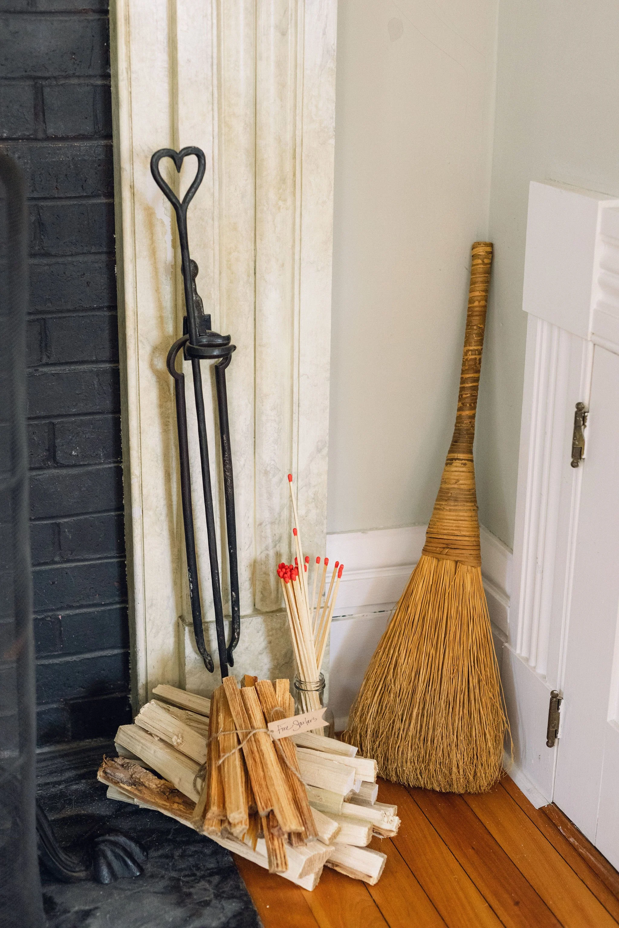 A collection of fireplace tools, firewood, and a broom in the corner of a room.