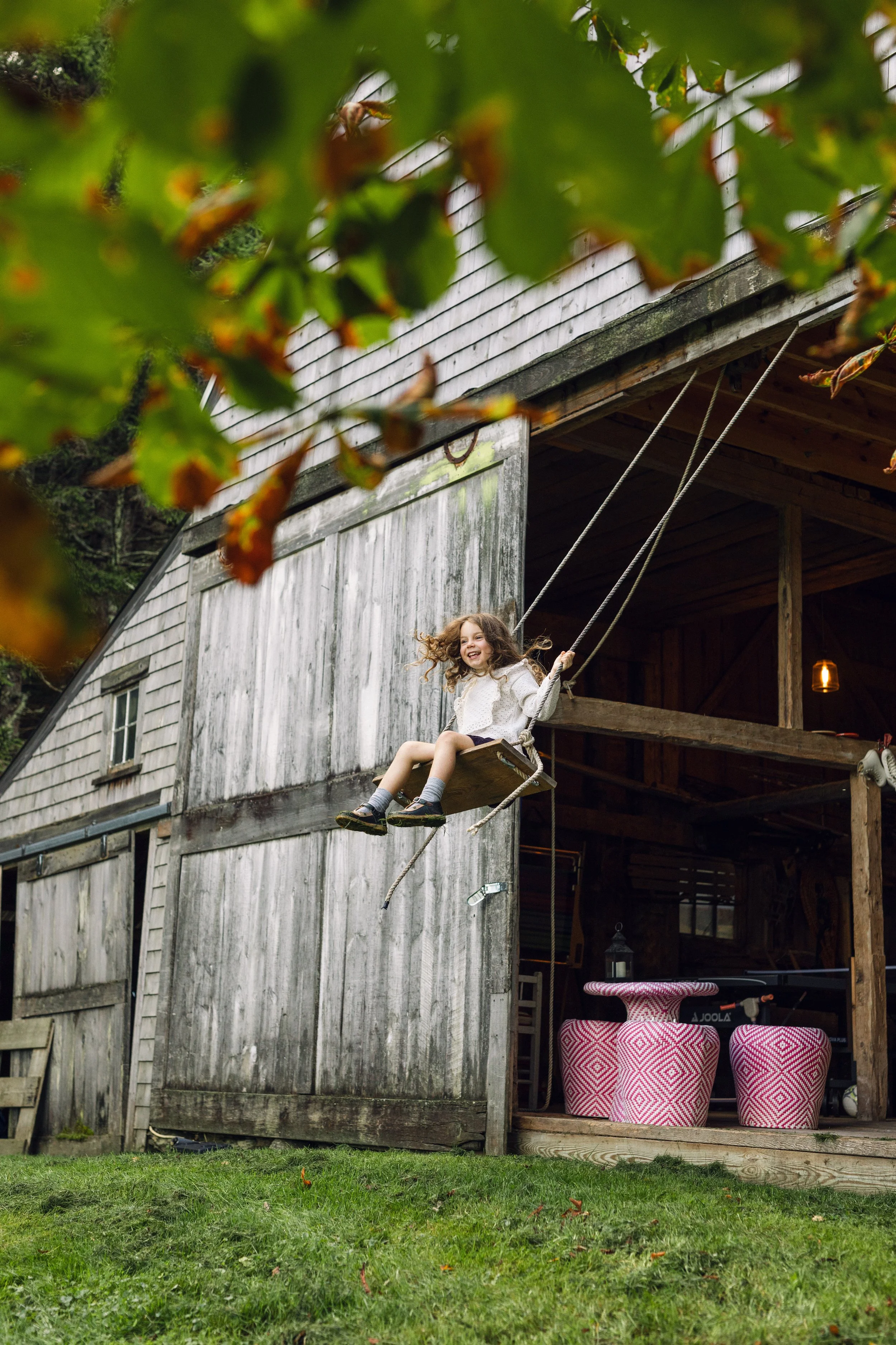 A girl on a wooden barn swing in a barn in Friendship, Maine.