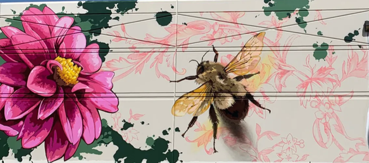 A mural featuring a large pink flower and a realistic bee with yellow and black markings, set against a background of pink floral outlines and green splatters.