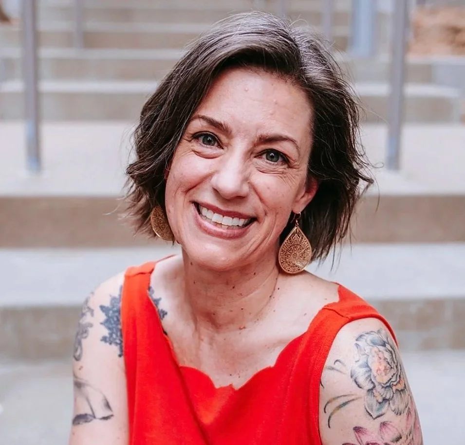A woman seated on a backwards chair facing forward smiling