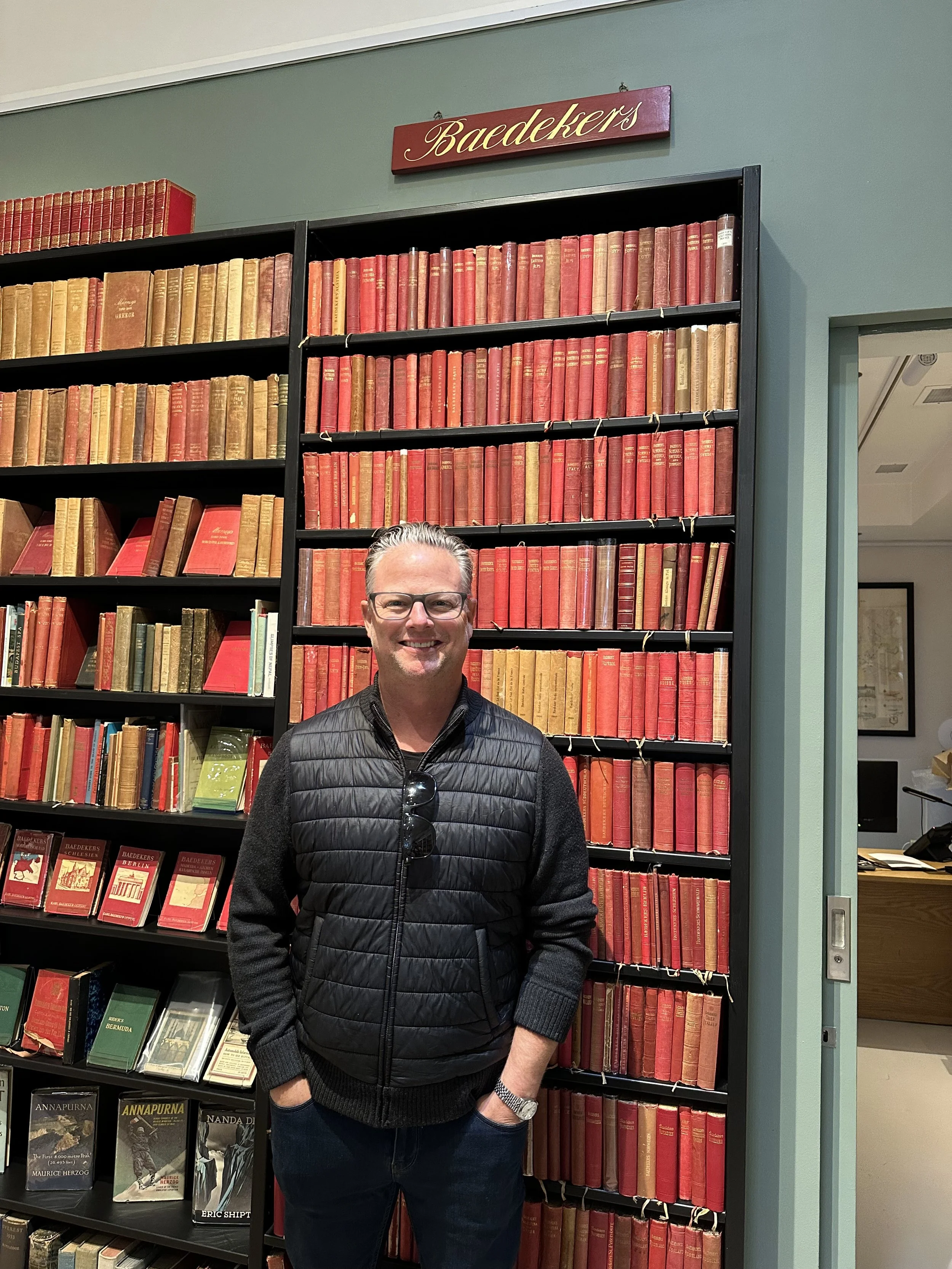 Peter Baedeker standing in front of a bookshelf of ancient Baedeker Guide Books at Shapero Rare Books in London.