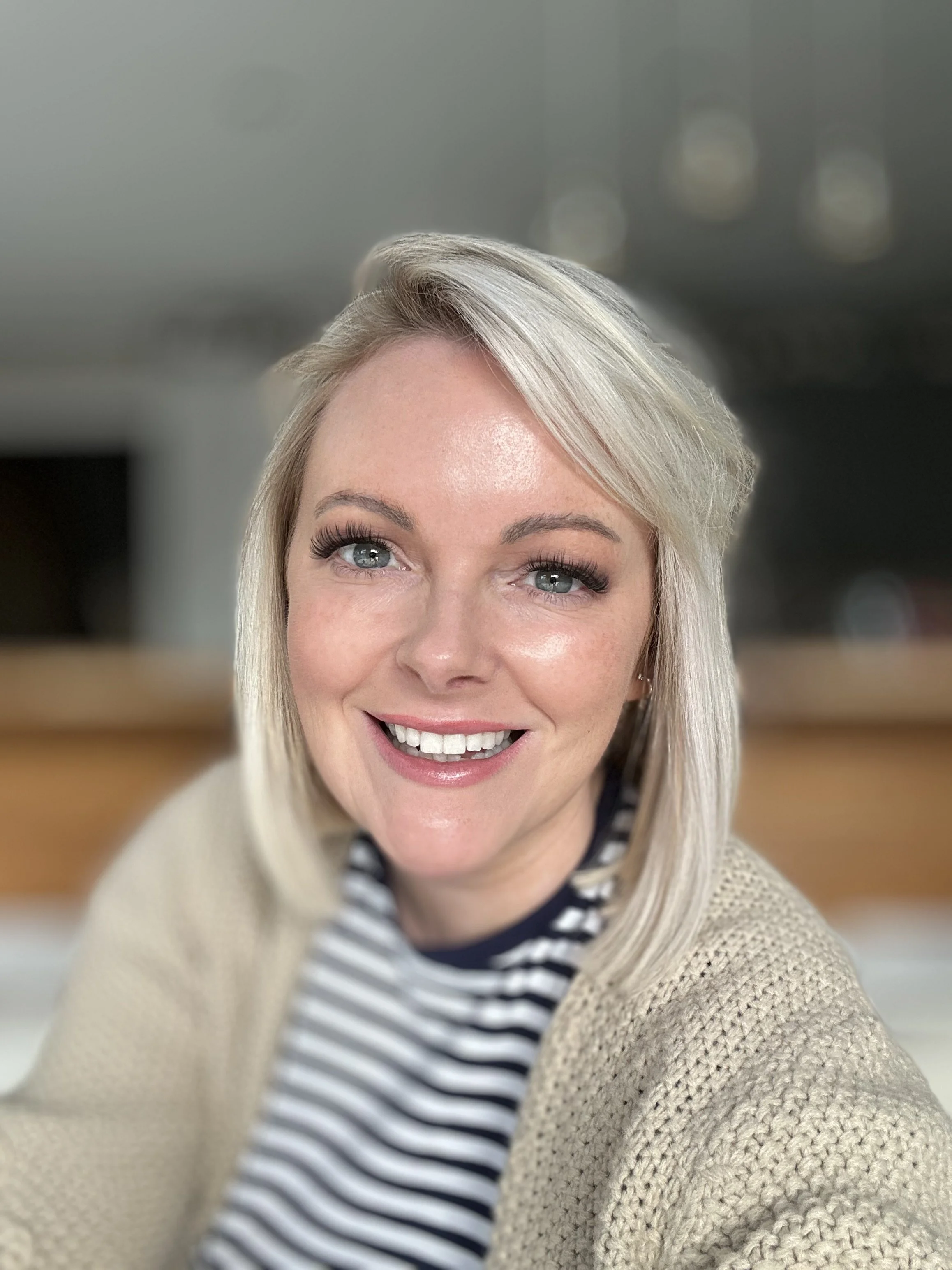 Smiling person in a striped shirt taking a selfie indoors.