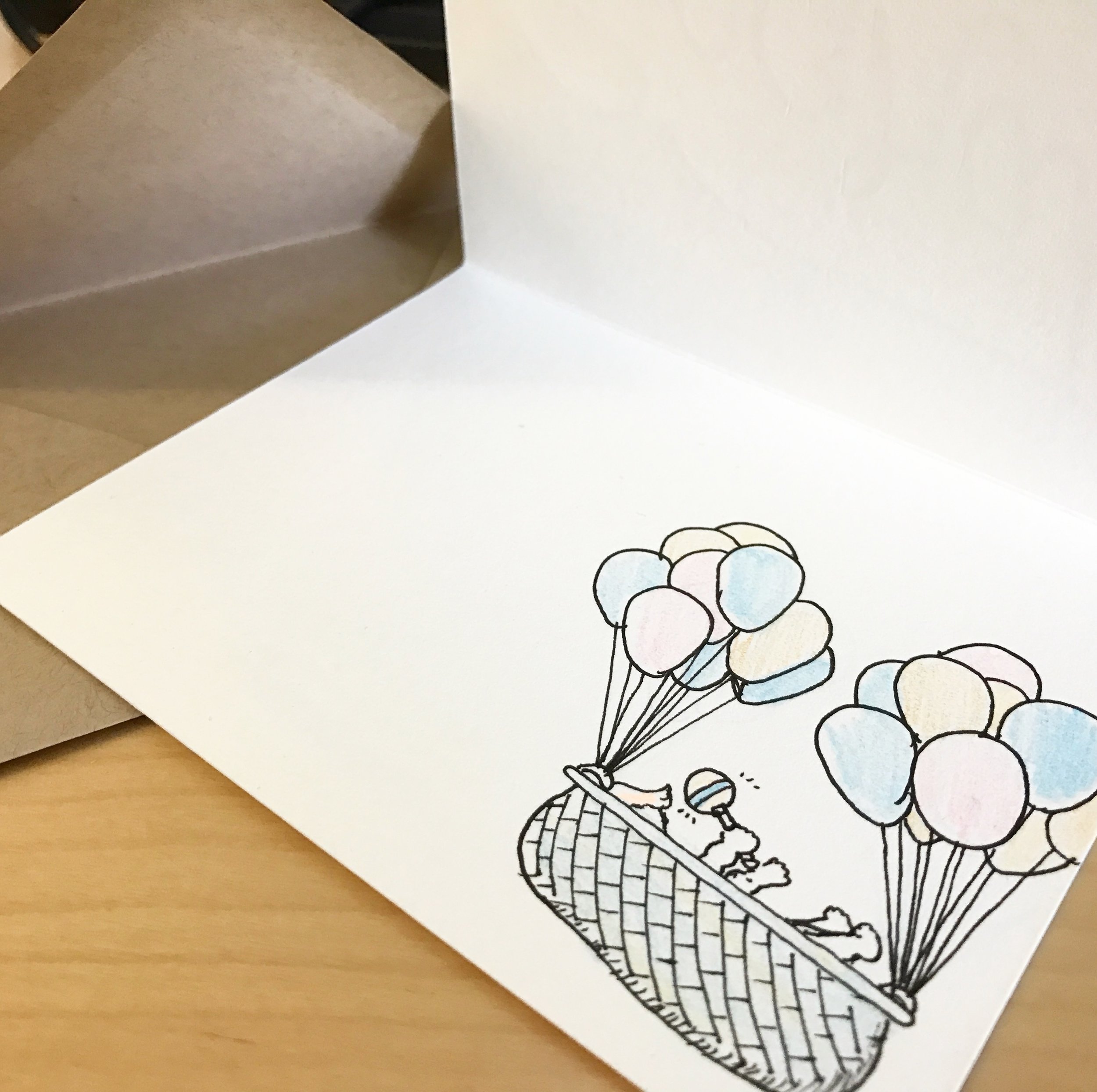 A woven baby basket is help aloft by many balloons. A baby's feet, hands, rattle, and tip of hair are peeking out from the basket top