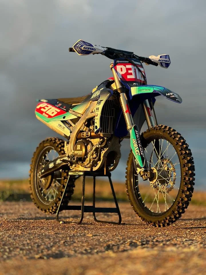 Off-road dirt bike with racing number P316 and Kawasaki branding, placed on a stand outdoors during daytime under a cloudy sky.