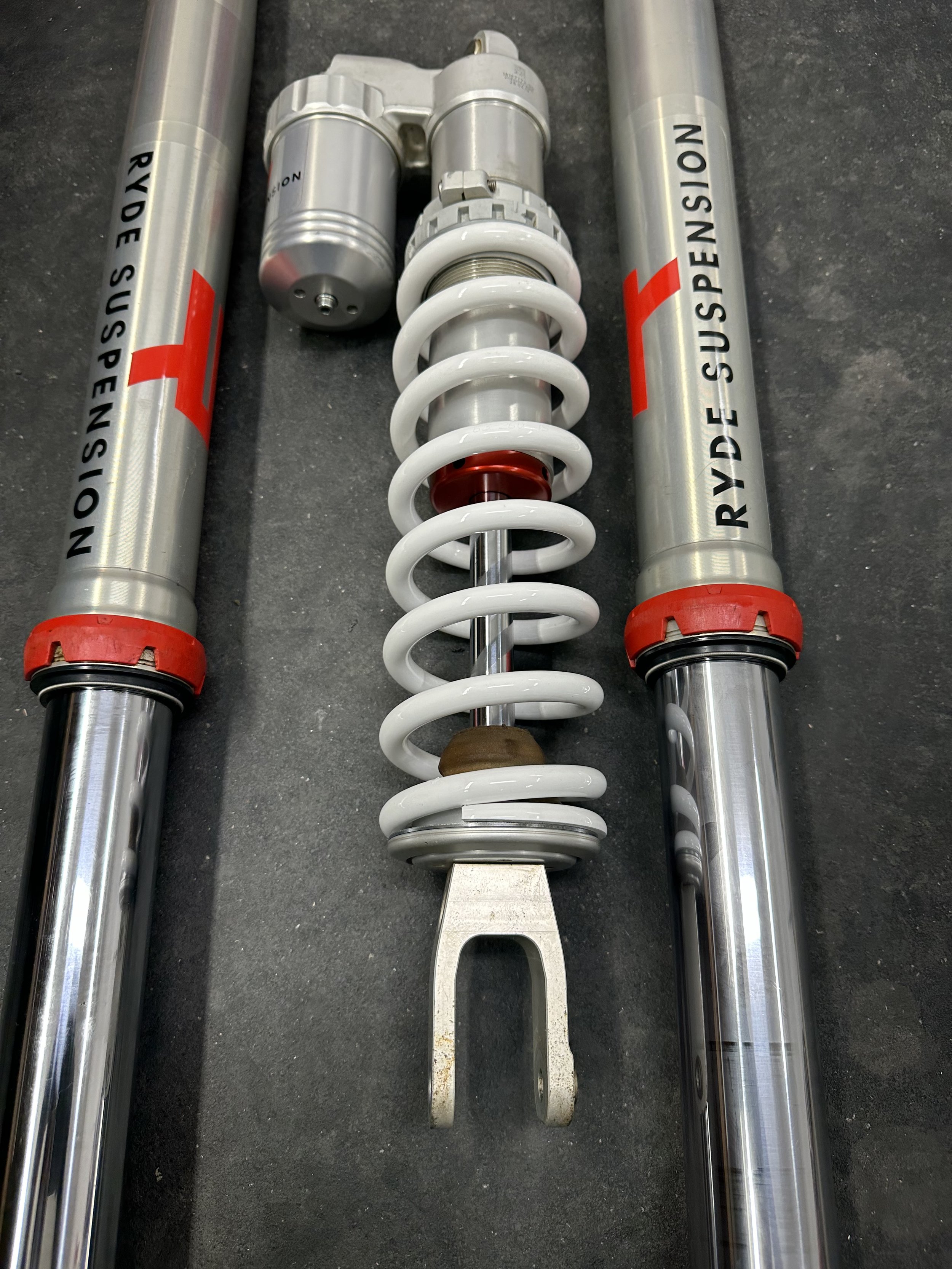 Motorcycle front suspension components, including two shock absorbers with labels, and a coil spring.