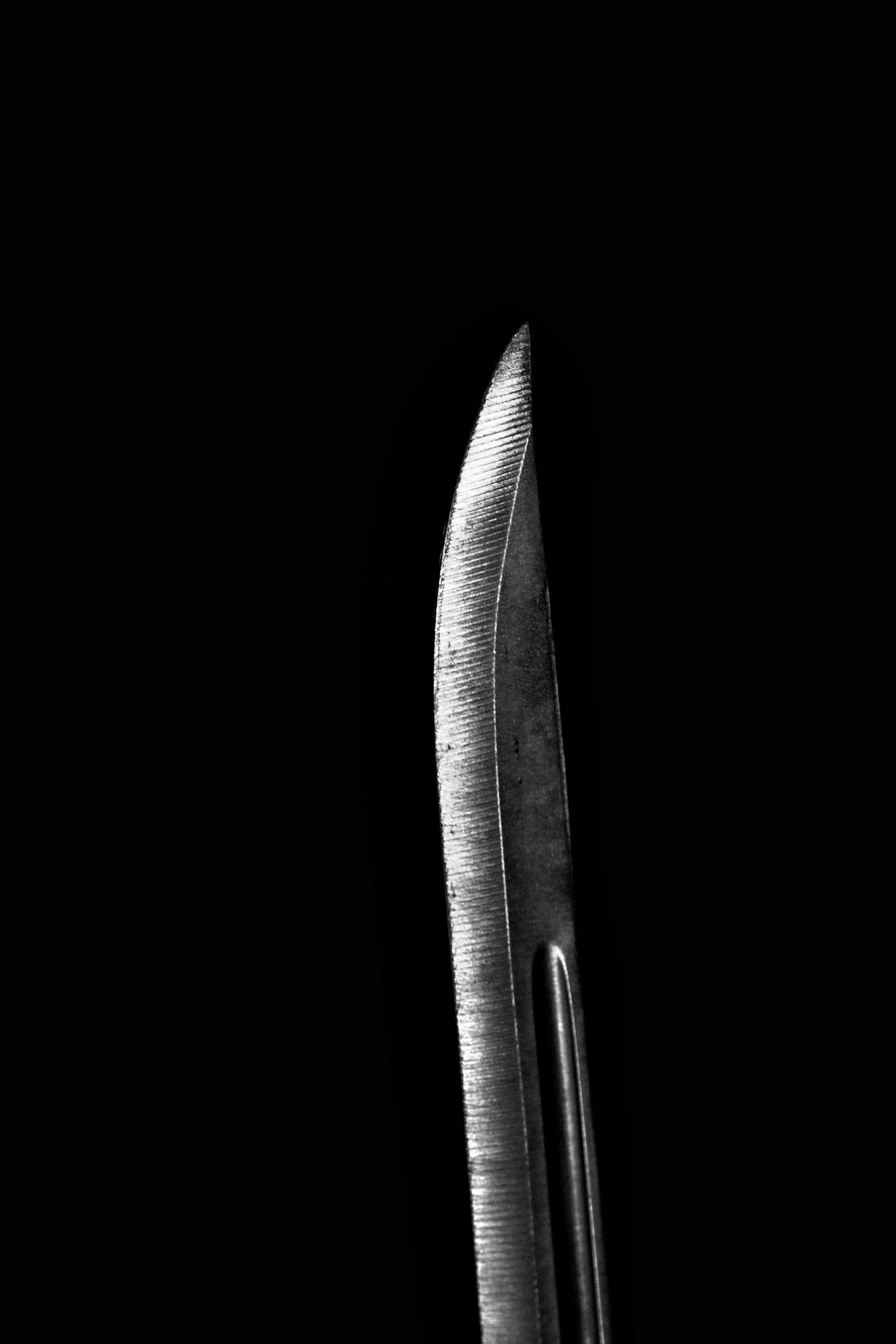 Close-up of a surgical scalpel with a sharp, pointed blade against a black background.