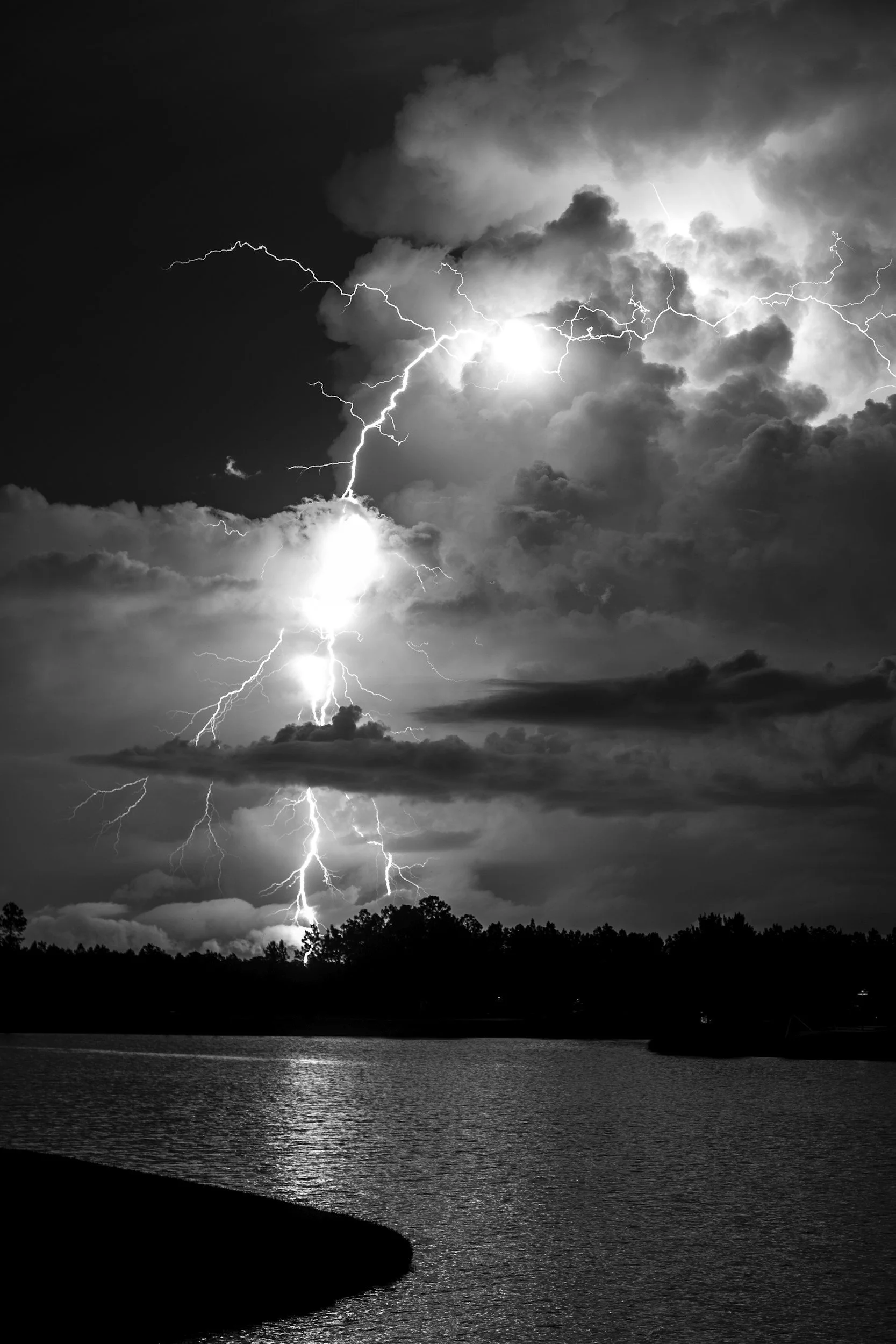 Black and white photo of a thunderstorm over a body of water, with visible lightning bolts and dark dramatic clouds.