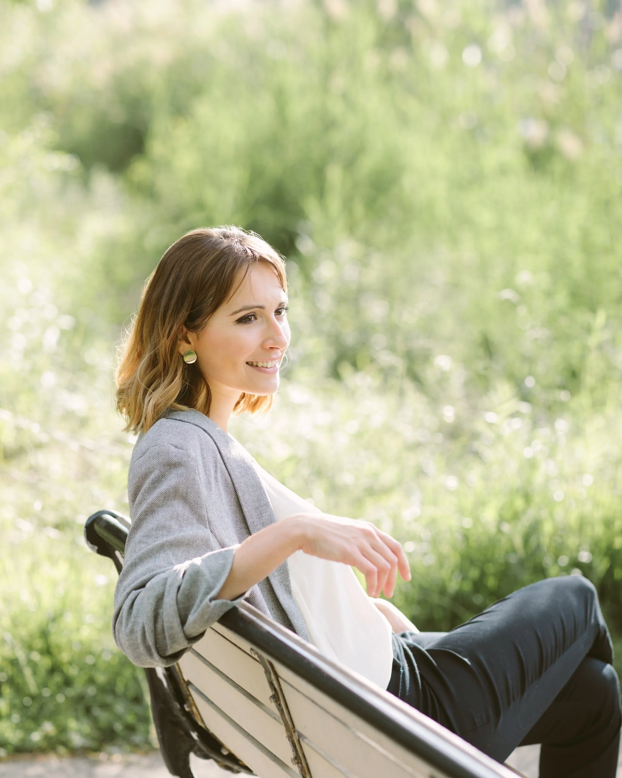 Woman sitting on a bench and looking away with greenery in the background