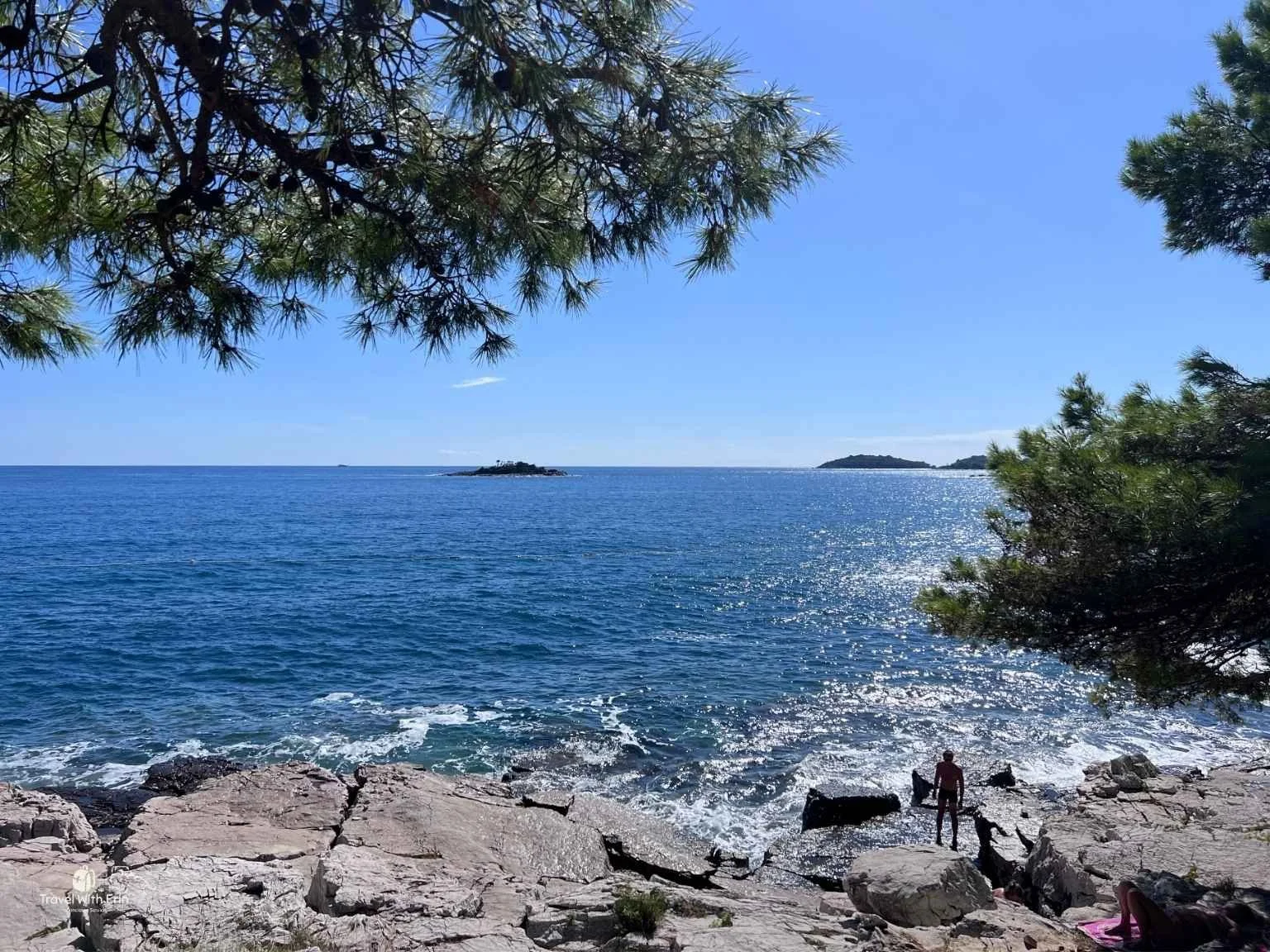 天氣晴朗的羅維尼海岸線，人們在岩石上曬太陽看海。