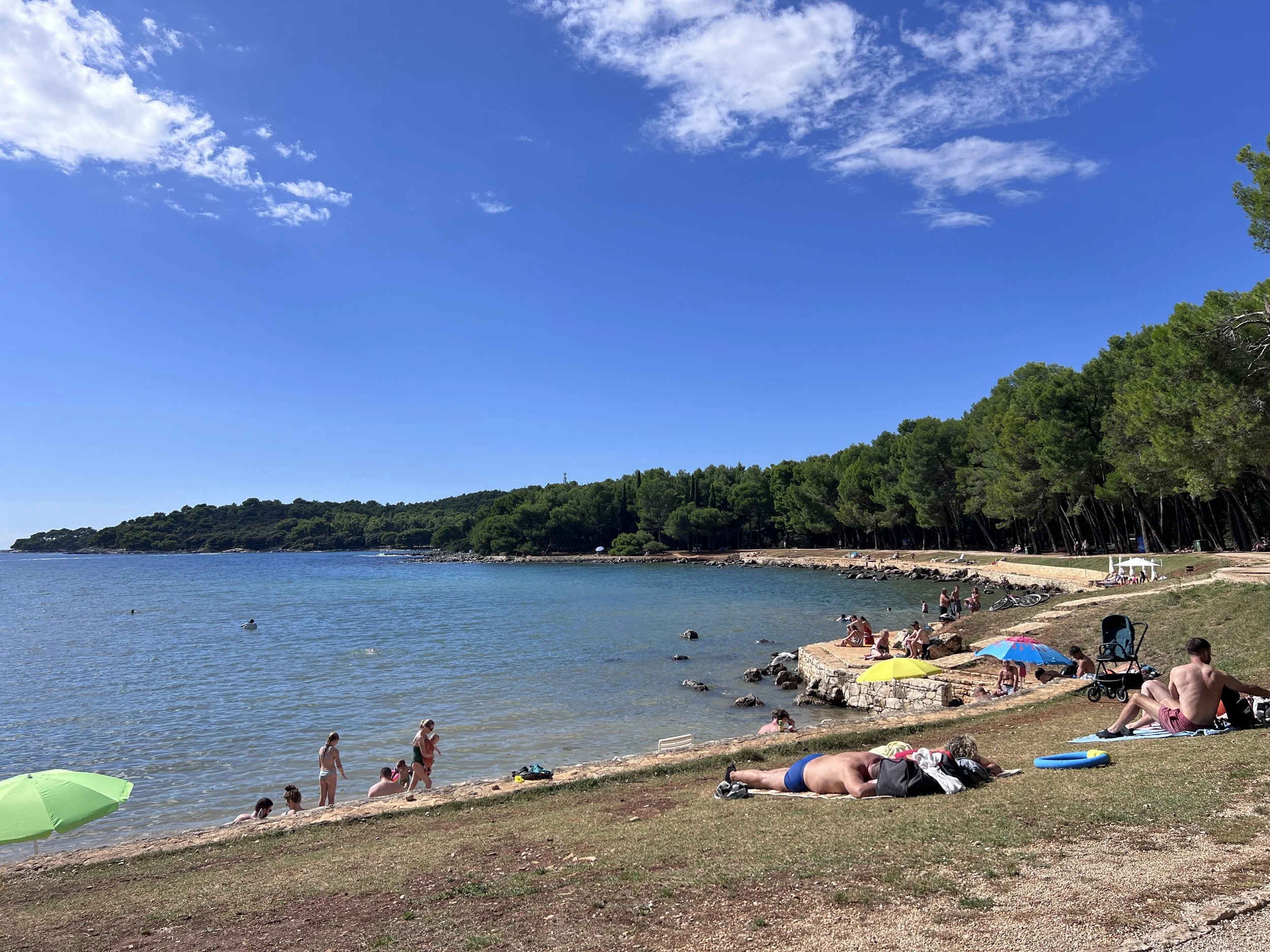 羅維尼海岸線上，人們在陽光下悠閒地曬太陽與游泳。