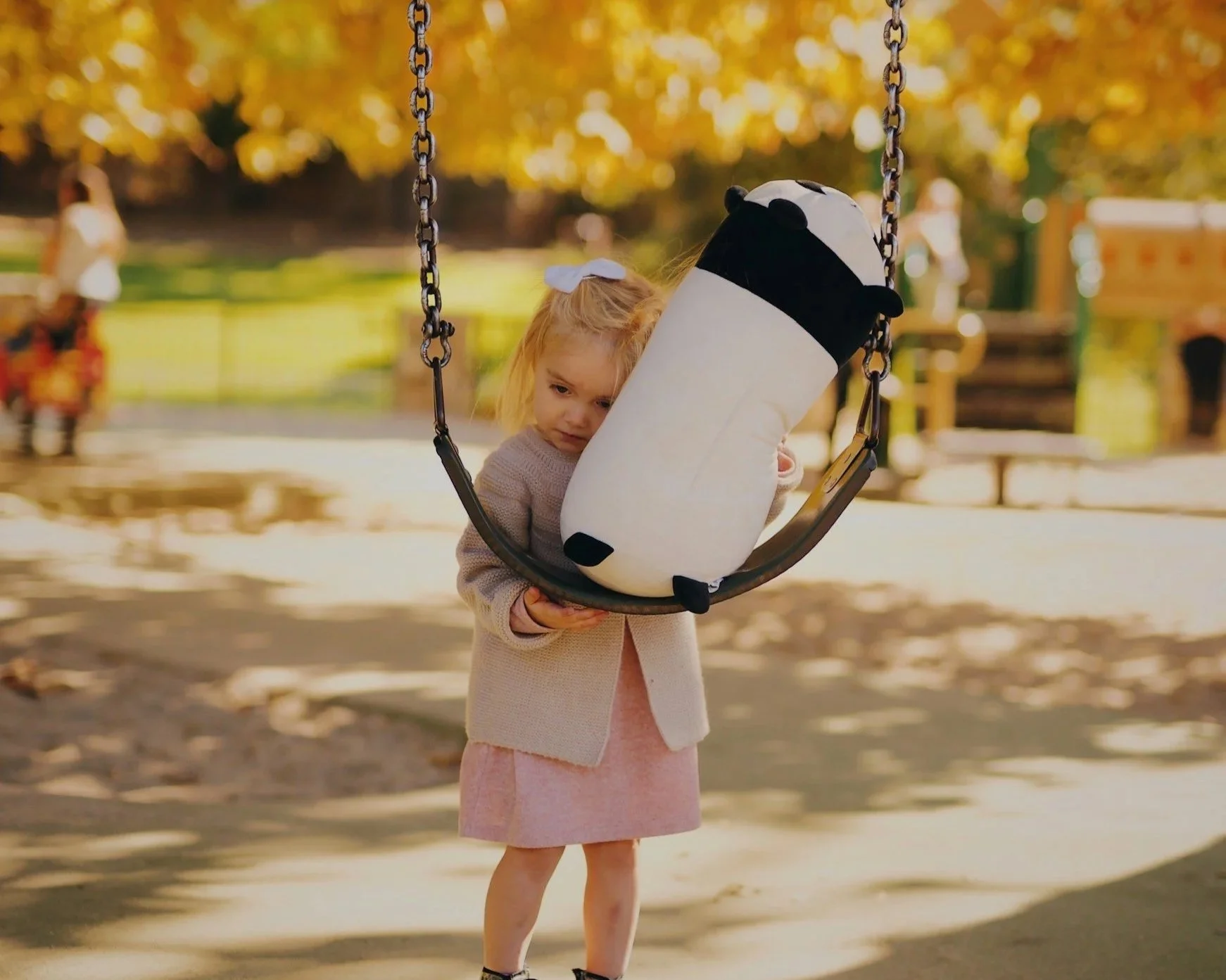 A sad looking girl hugging a toy by the swing