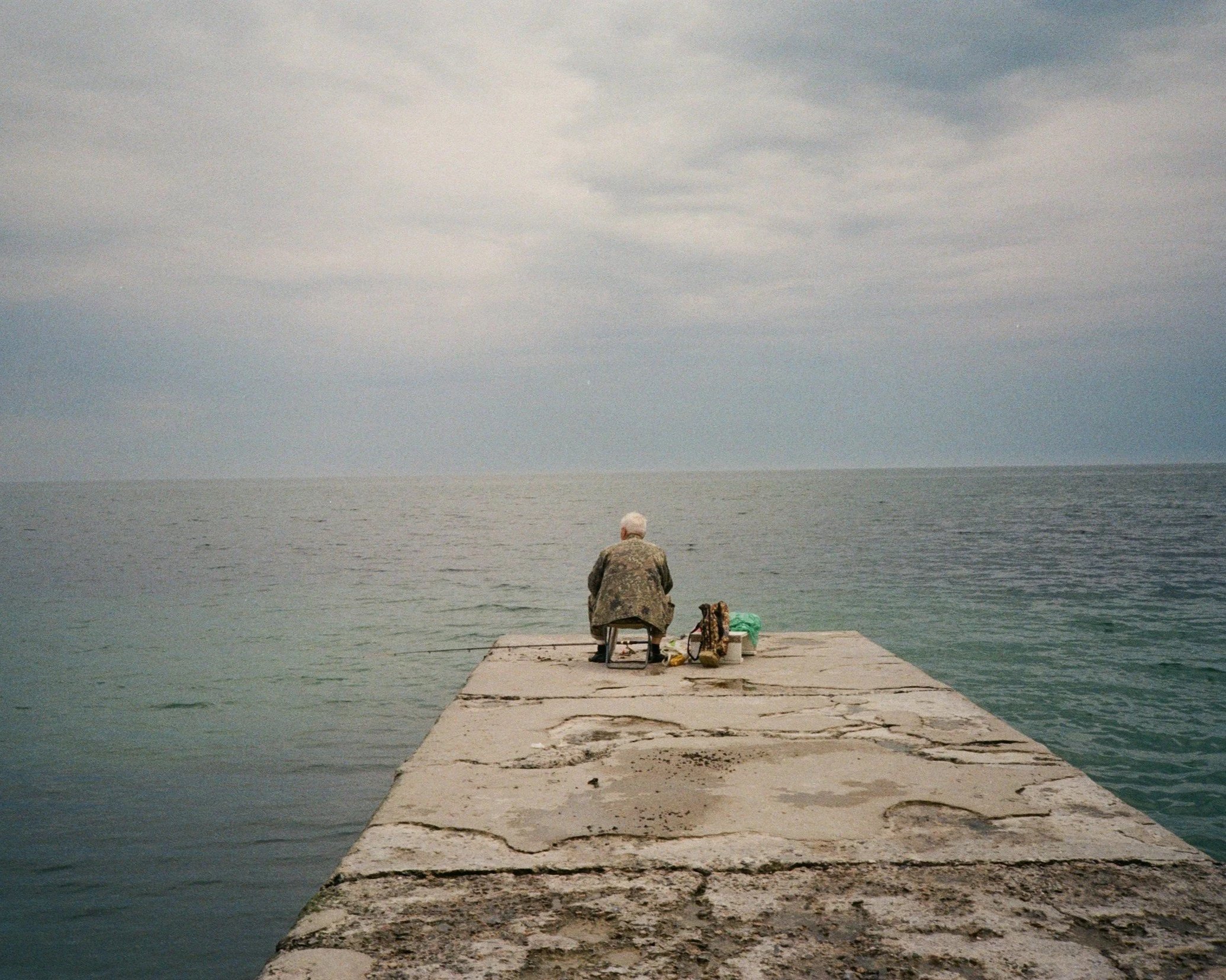 Person sitting alone at the end of a pier, facing open water