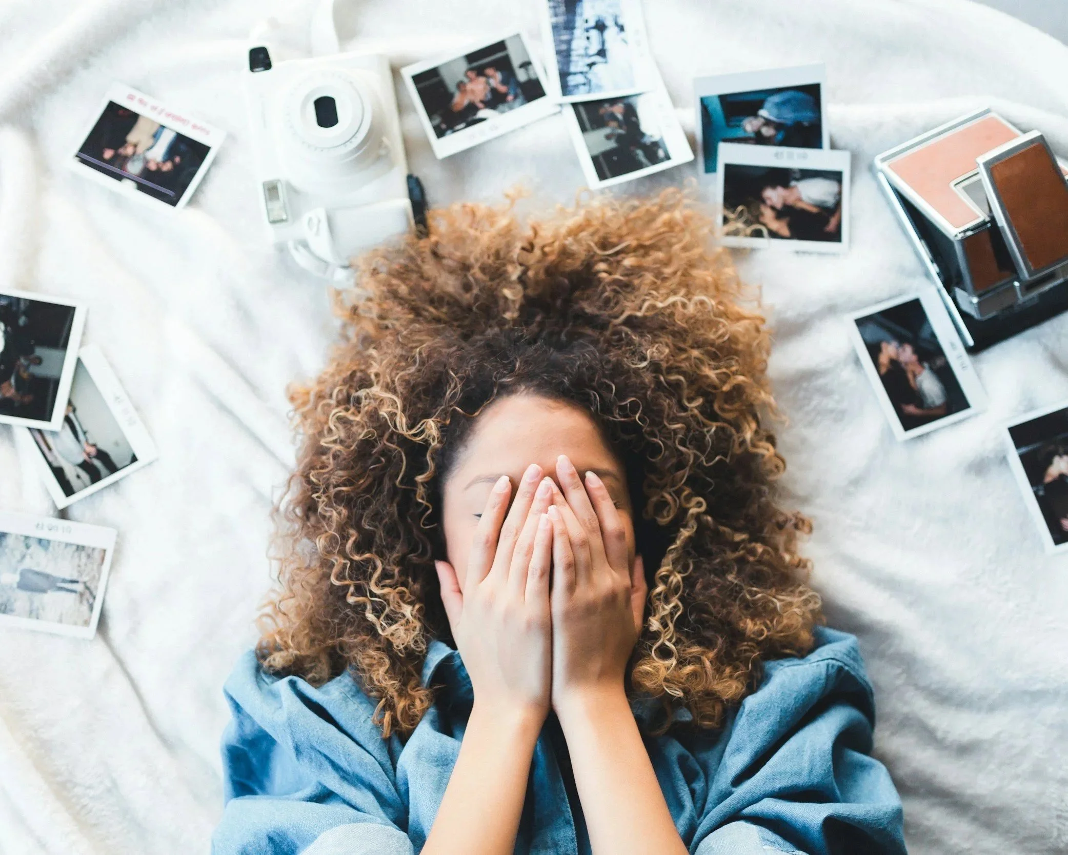 Woman on a bed, hididng her face, surrounded by photos