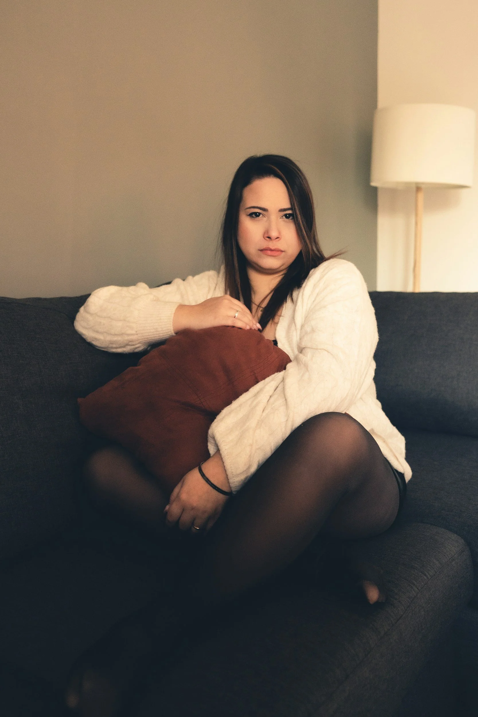 Woman sitting on a sofa holding a large cushion protectively against her body, illustrating the emotional vulnerability and uncertainty often felt in relationship anxiety.
