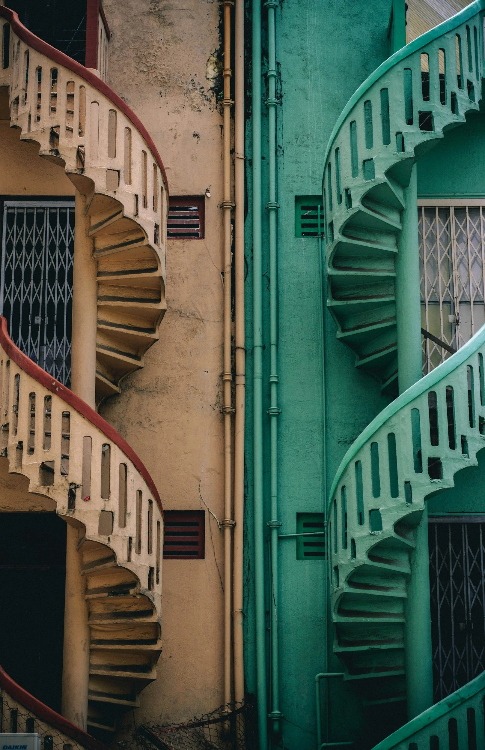 Mirrored images of a spiral staircase, one in warm orange tones and one in cooler green tones.