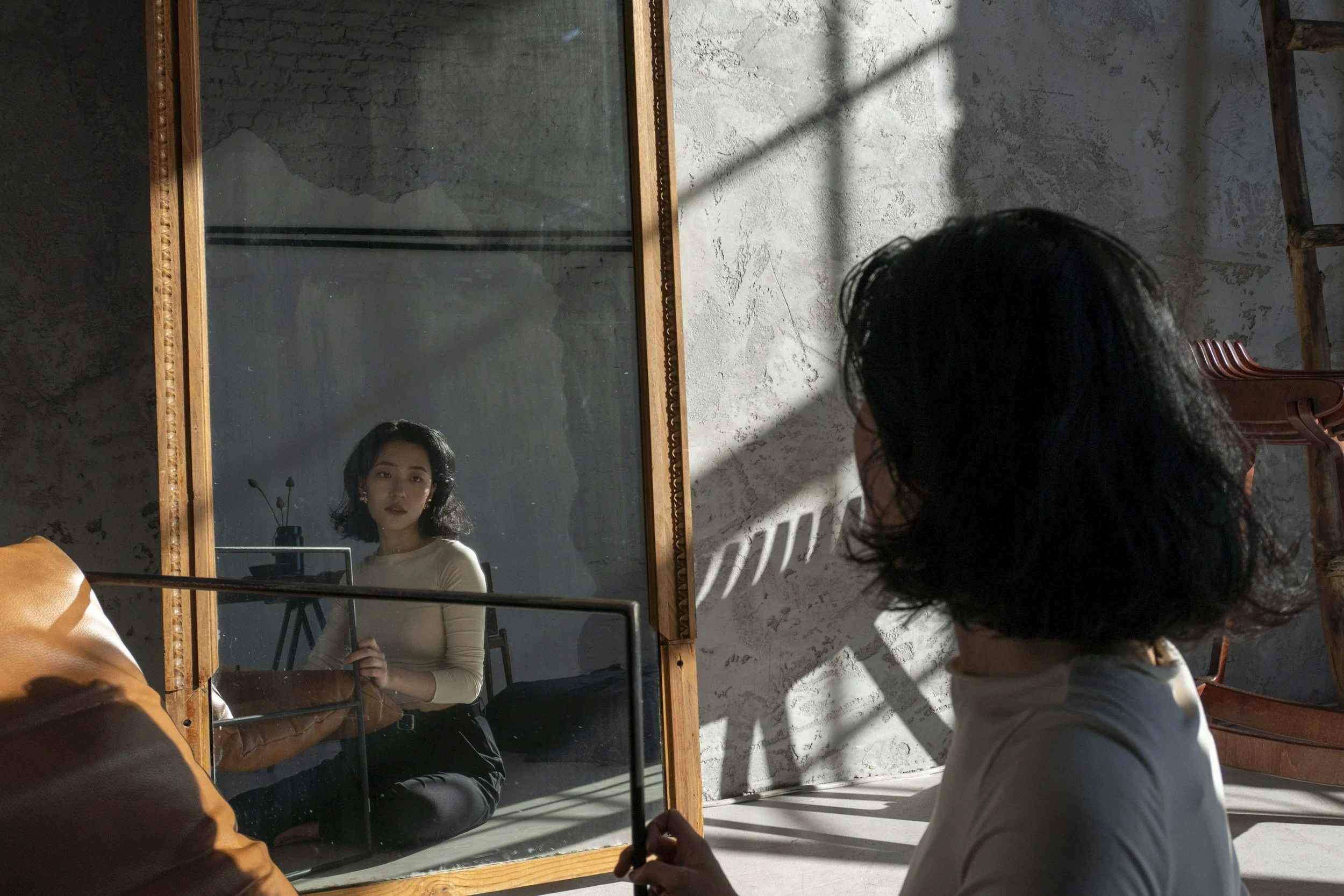 Woman sitting in front of a mirror, looking at her reflection in a quiet room