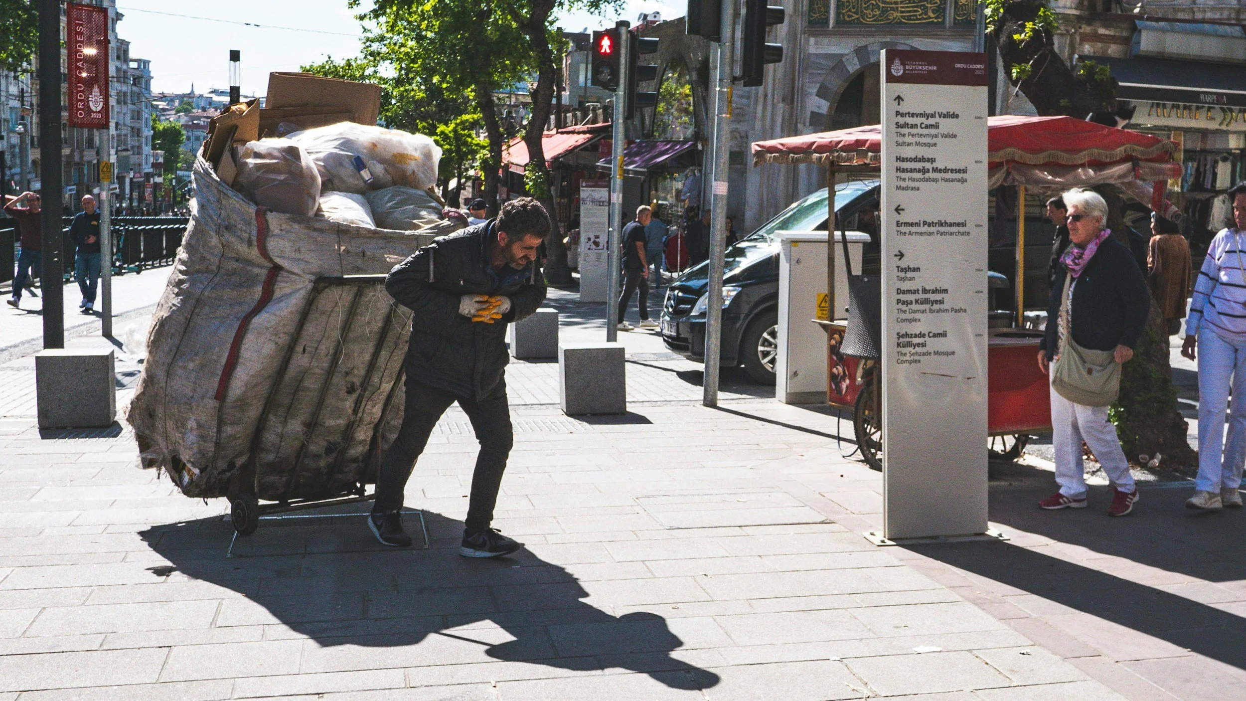 Man pulling an oversized, heavily loaded cart along a busy city street.