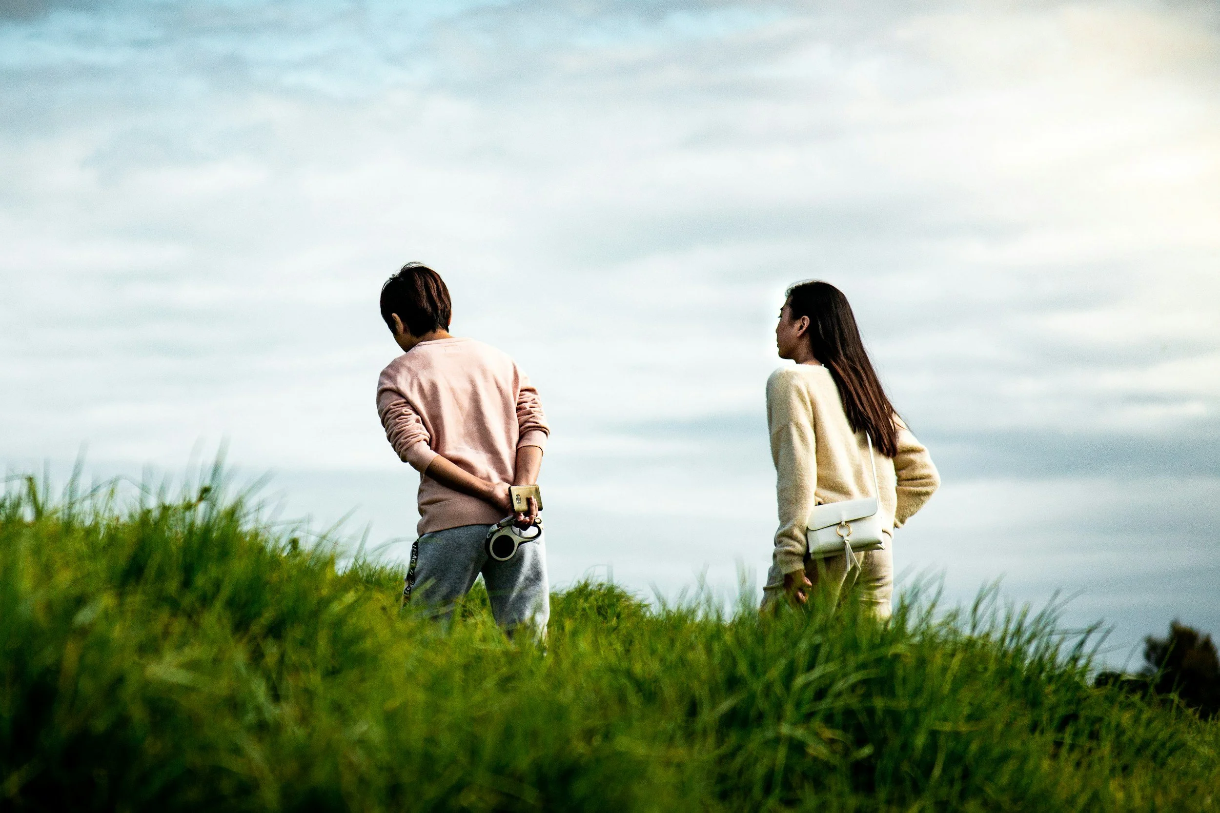 Two people standing apart in a grassy field, facing away from each other