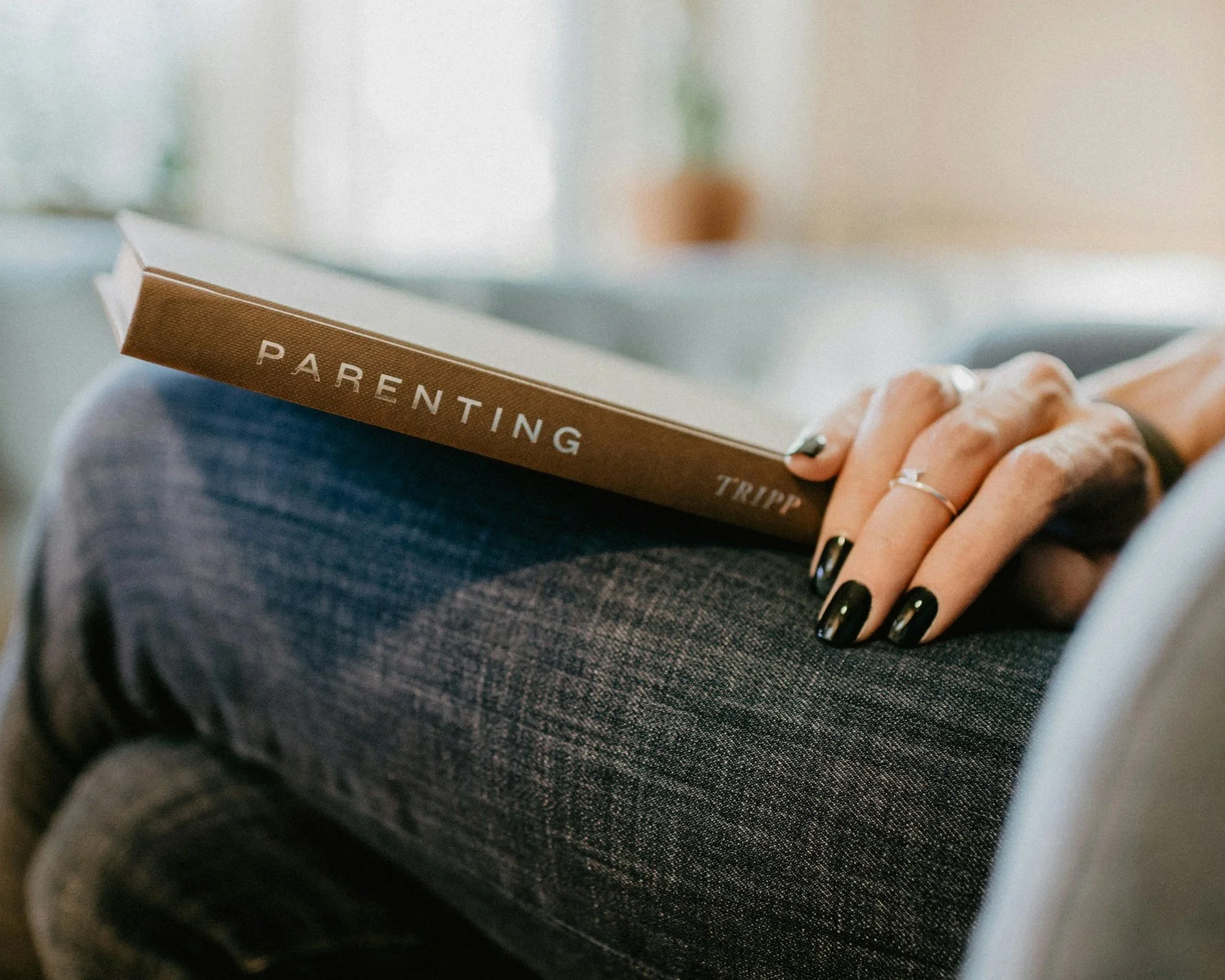 an image of a womens lower body sitting in a chair holdign a Parenting book
