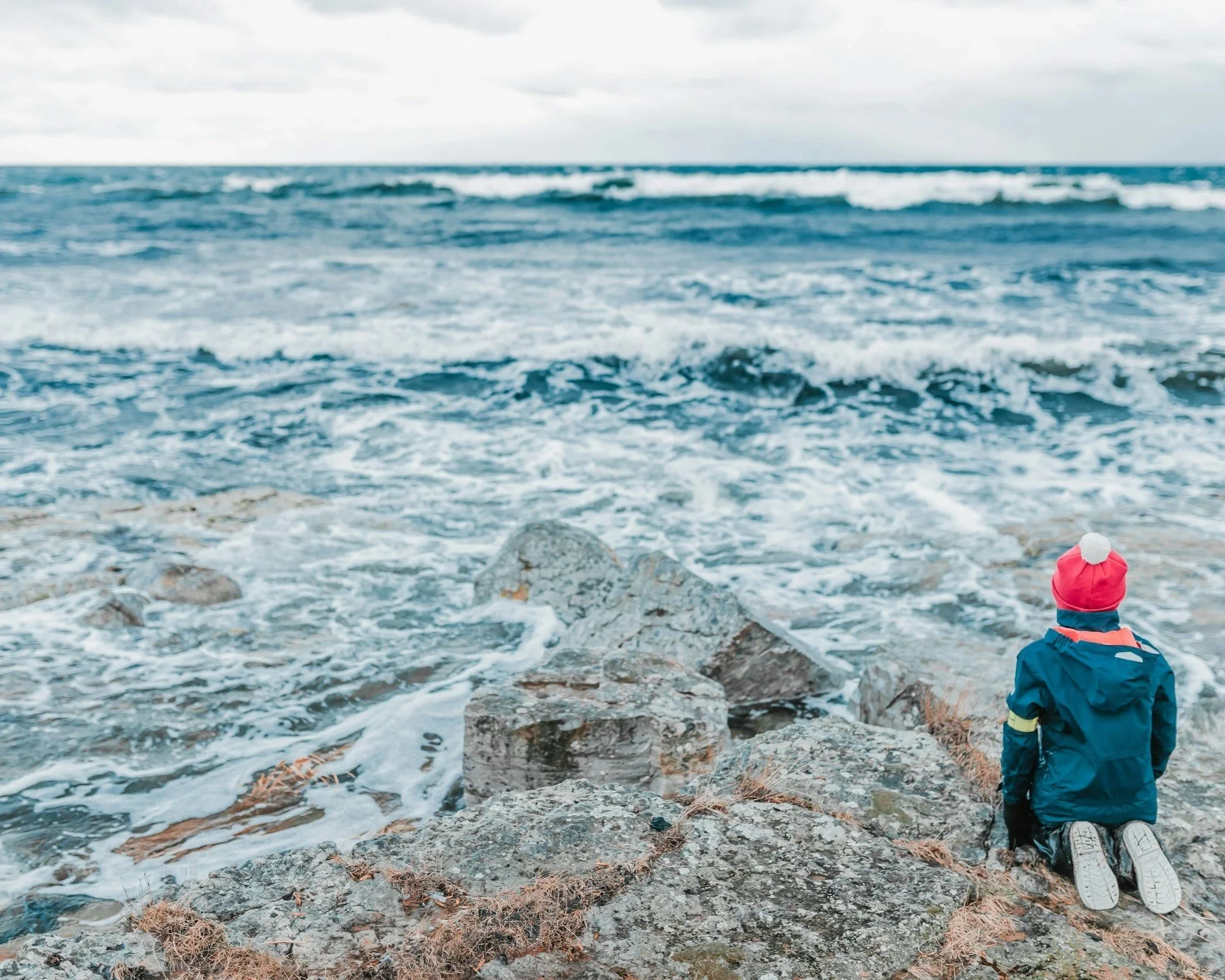 Child sitting by the ocean, looking out across the water