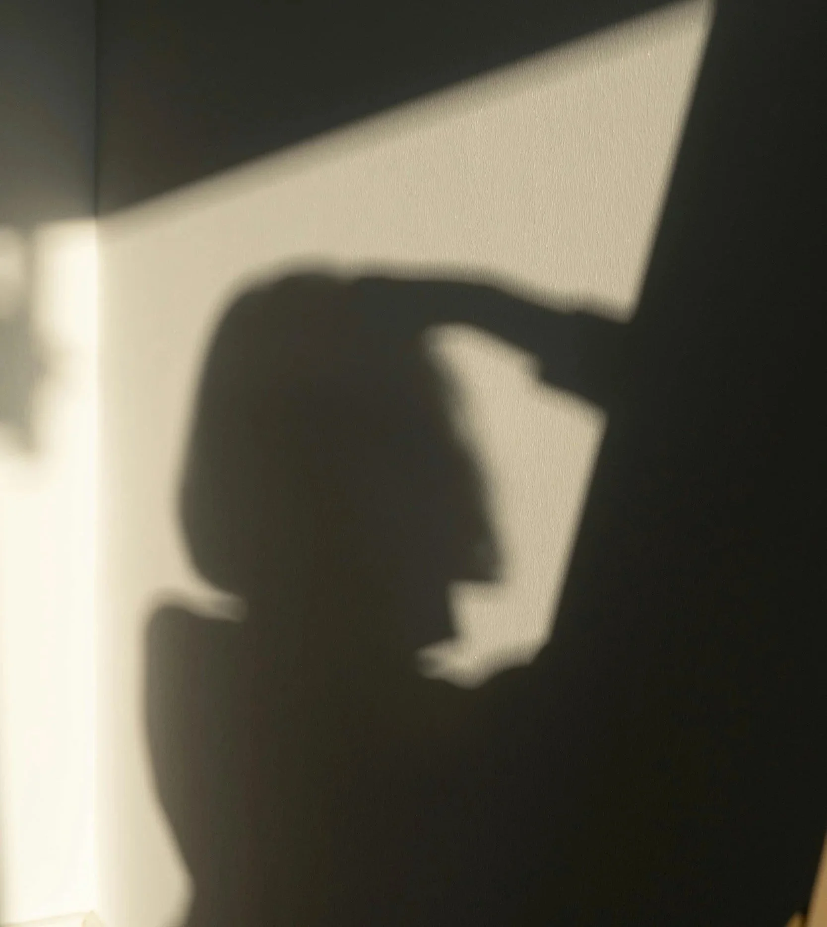 Silhouette of a person with hand to head in soft light, reflecting quietly