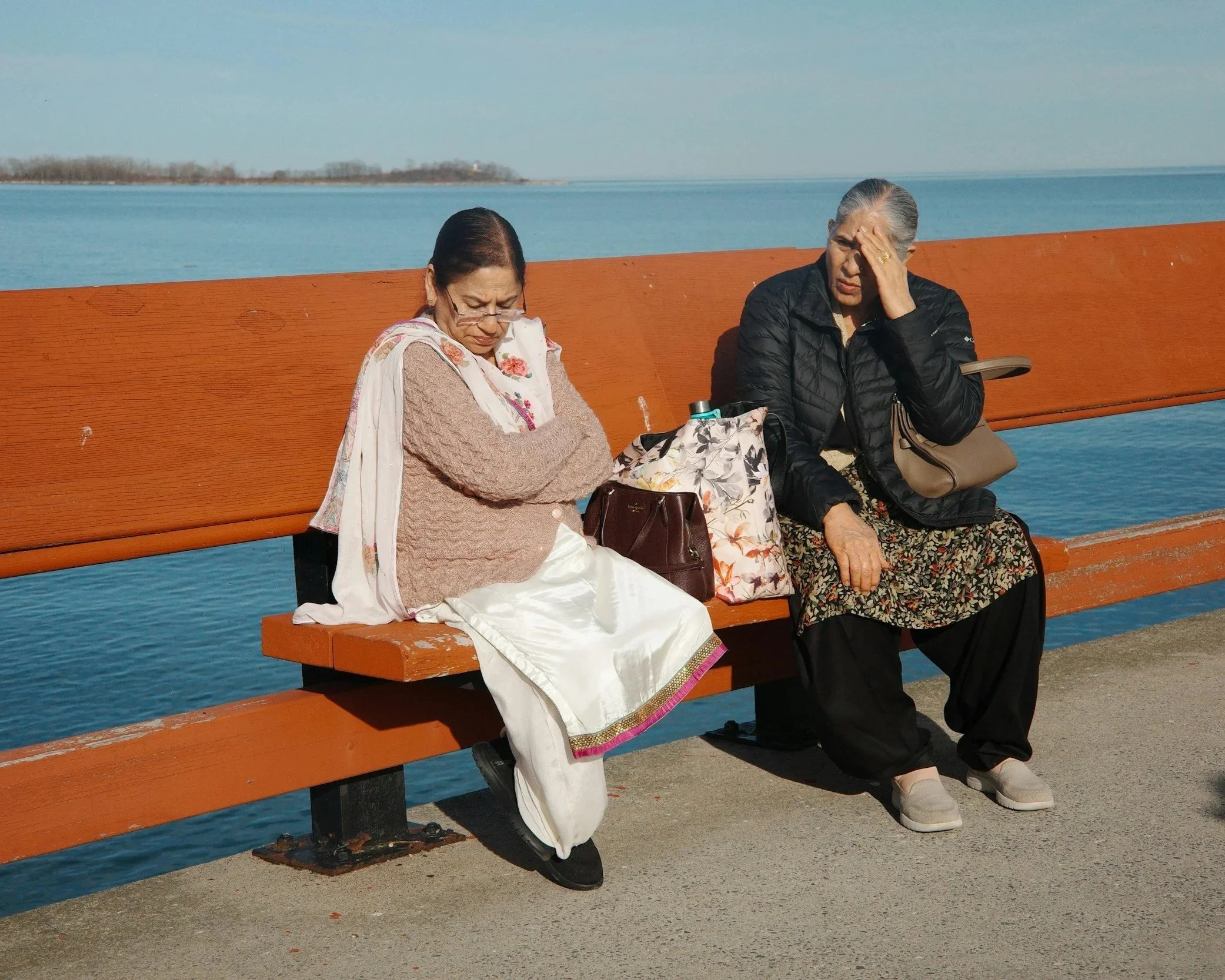 Two women sitting together on a bench, one looking away while the other speaks