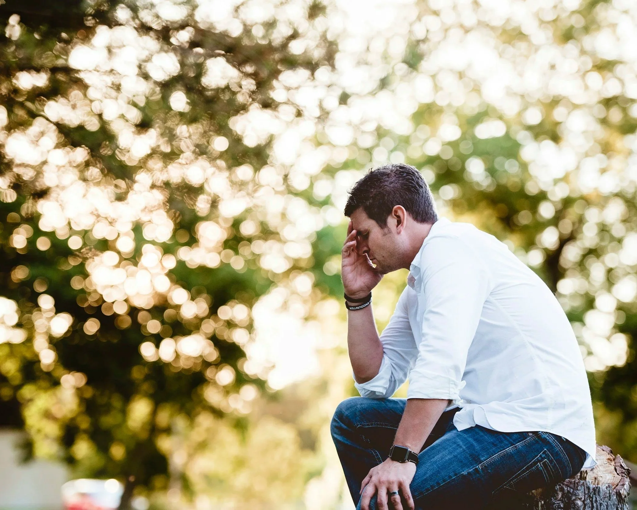 Man sitting alone outdoors with head in hands appearing emotionally overwhelmed.