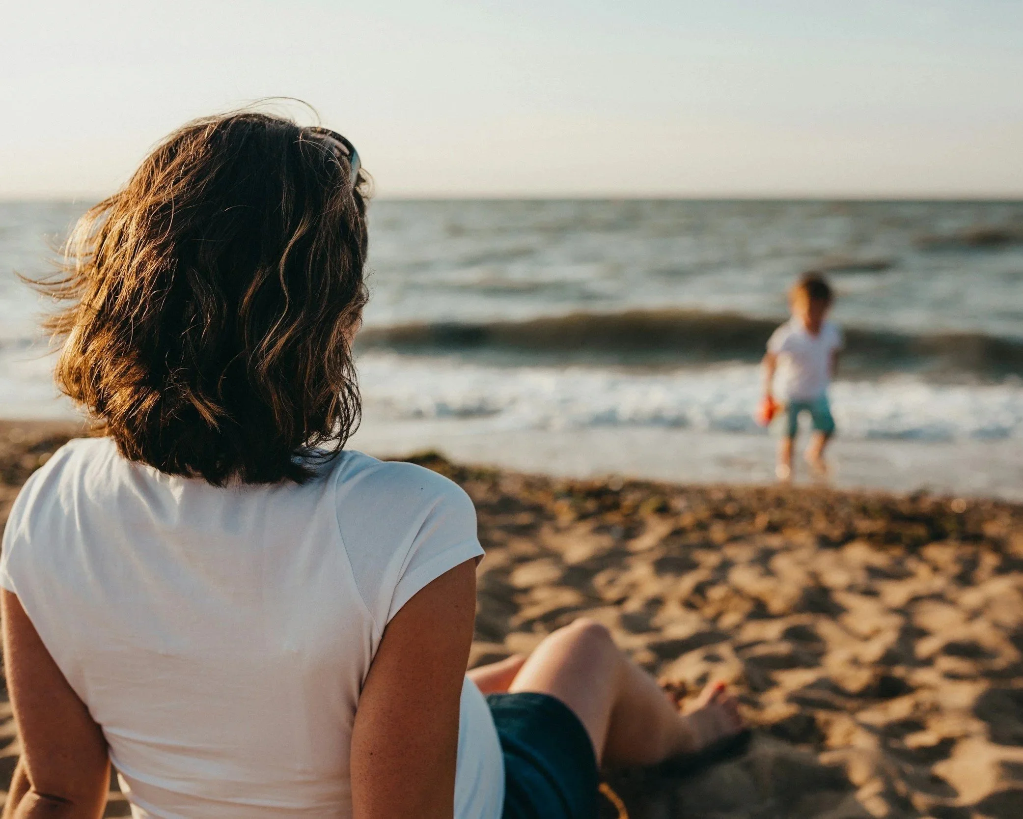 woman sitting alone on beach reflecting emotional neglect and maternal relationship wounds