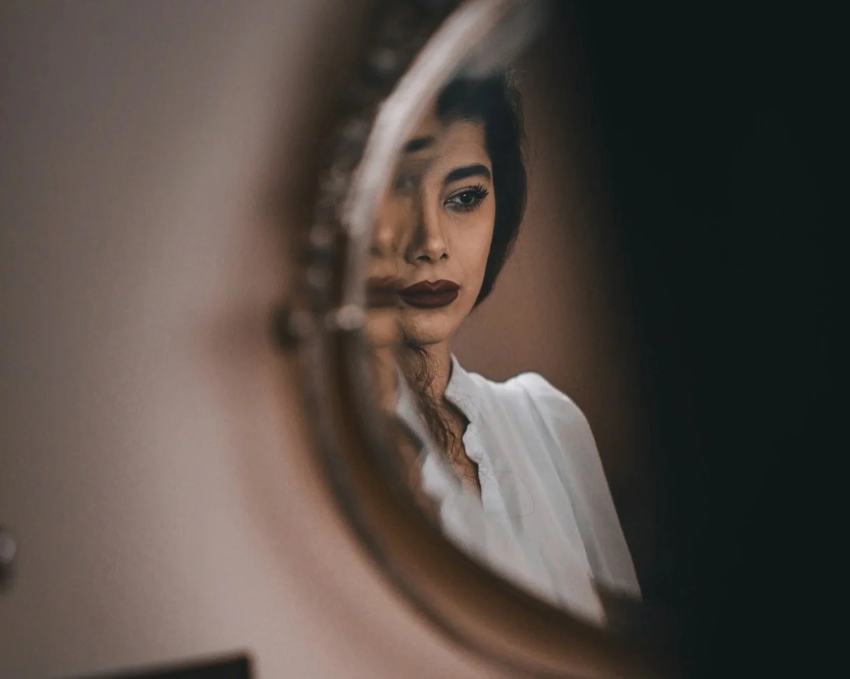 Woman looking into a mirror with blurred reflection symbolising self-doubt and gaslighting.