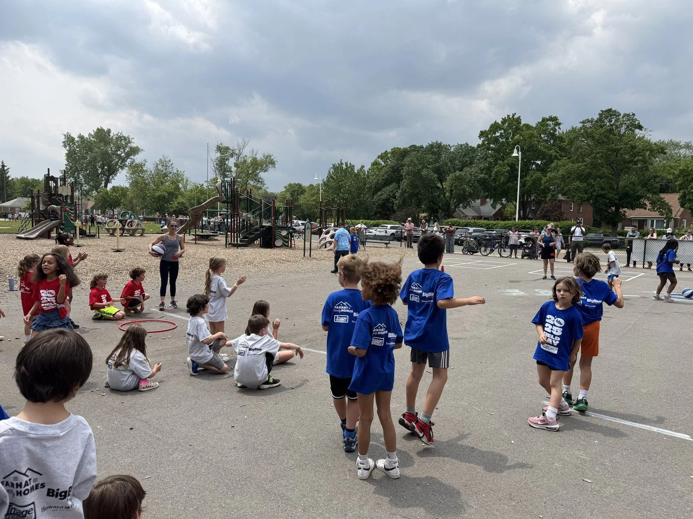 Kids playing outdoor games and sports on a playground and parking lot, with trees and cloudy sky in the background.