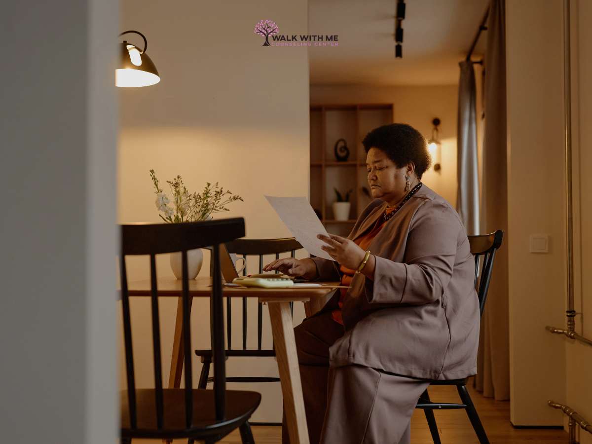 Black woman reviewing household paperwork with a notebook at a table.
