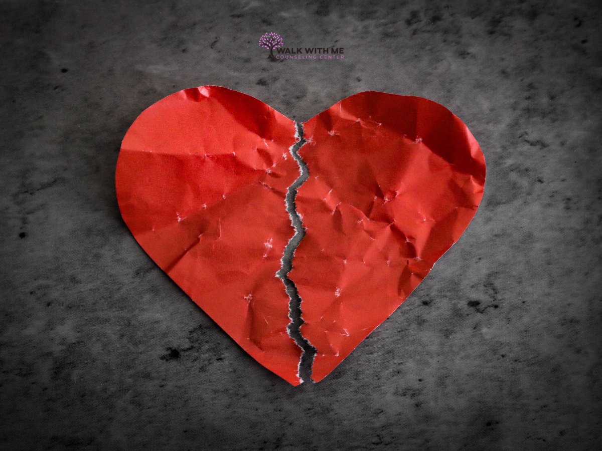 A torn, crumpled red paper heart representing the pain of a breakup.