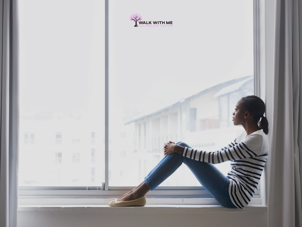 Black woman sitting near a window looking faraway