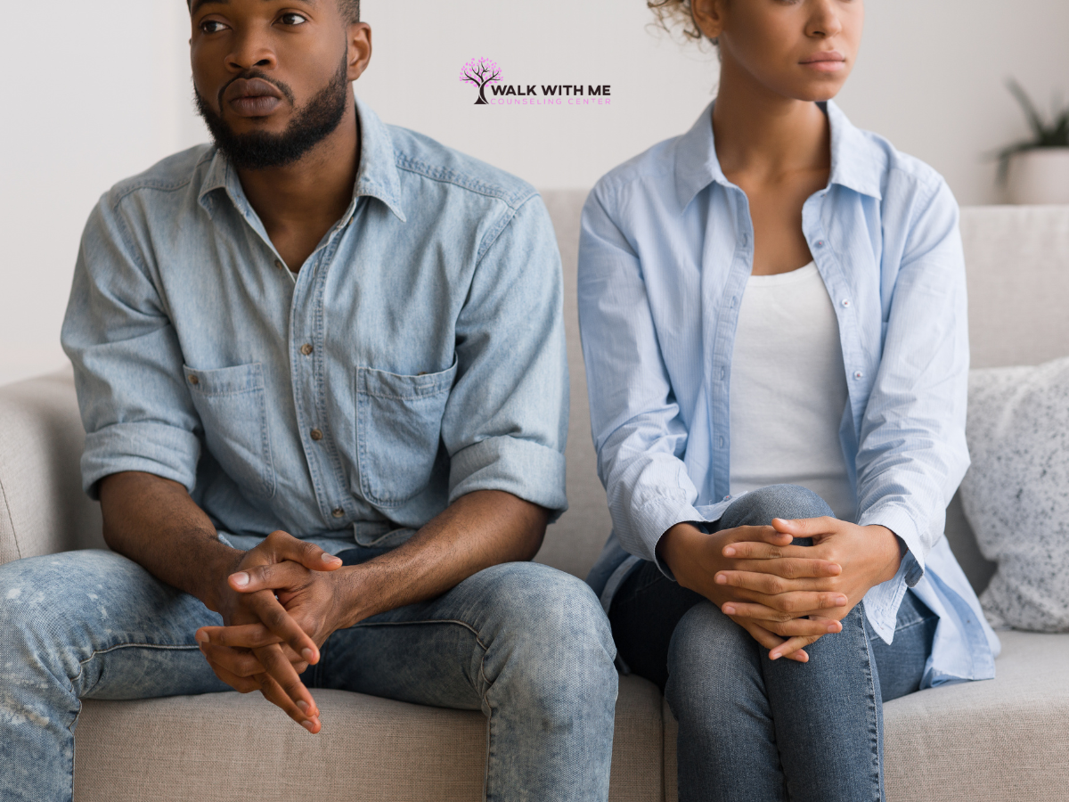 Couple sitting on opposite ends of a couch, one person looking away with a flat expression